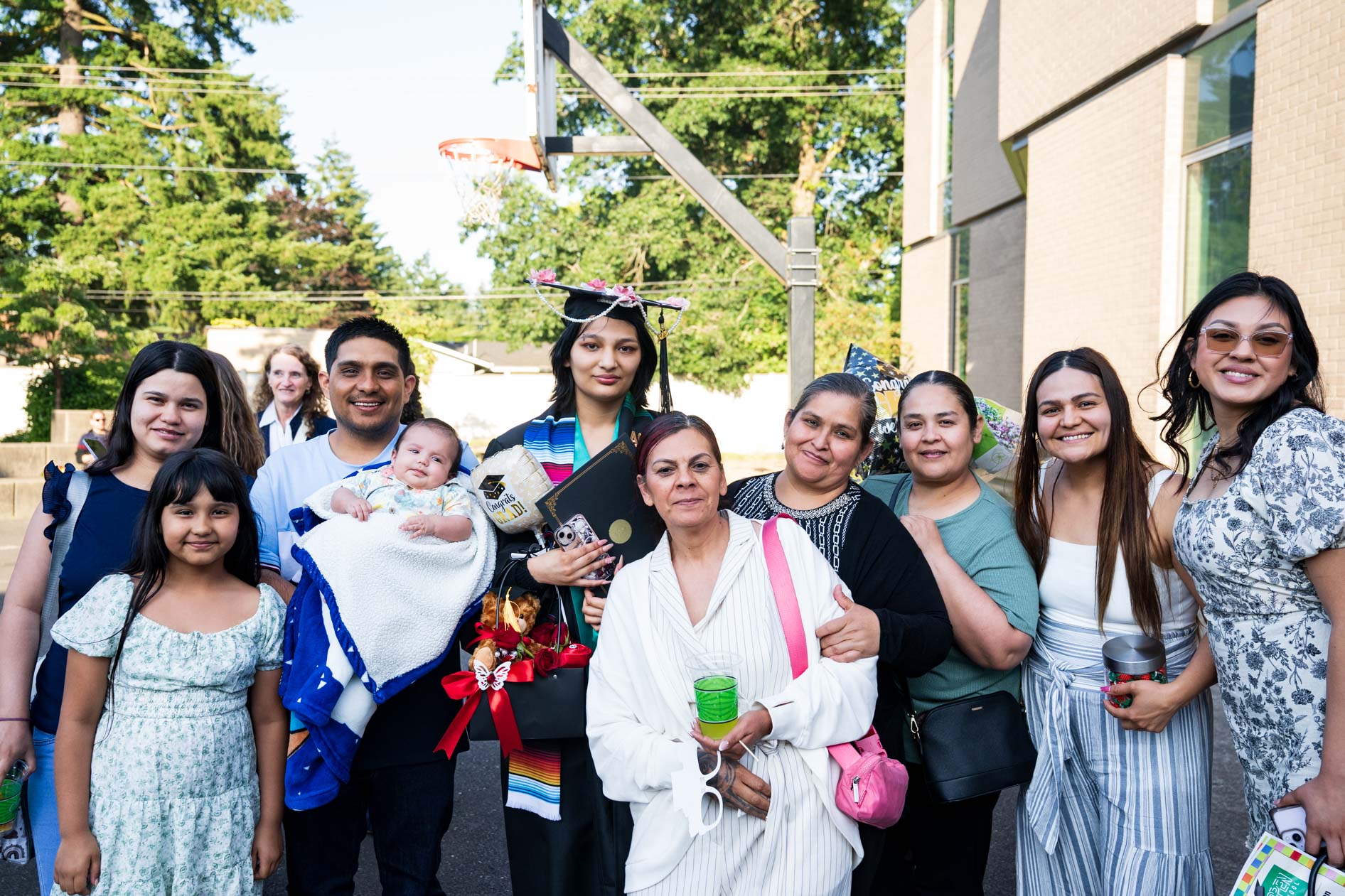 A large, multi-generational family poses for a group photo with a graduate in a cap and gown. This is an example of an event photographer in Portland, Oregon, capturing a joyful graduation moment for Open School East.