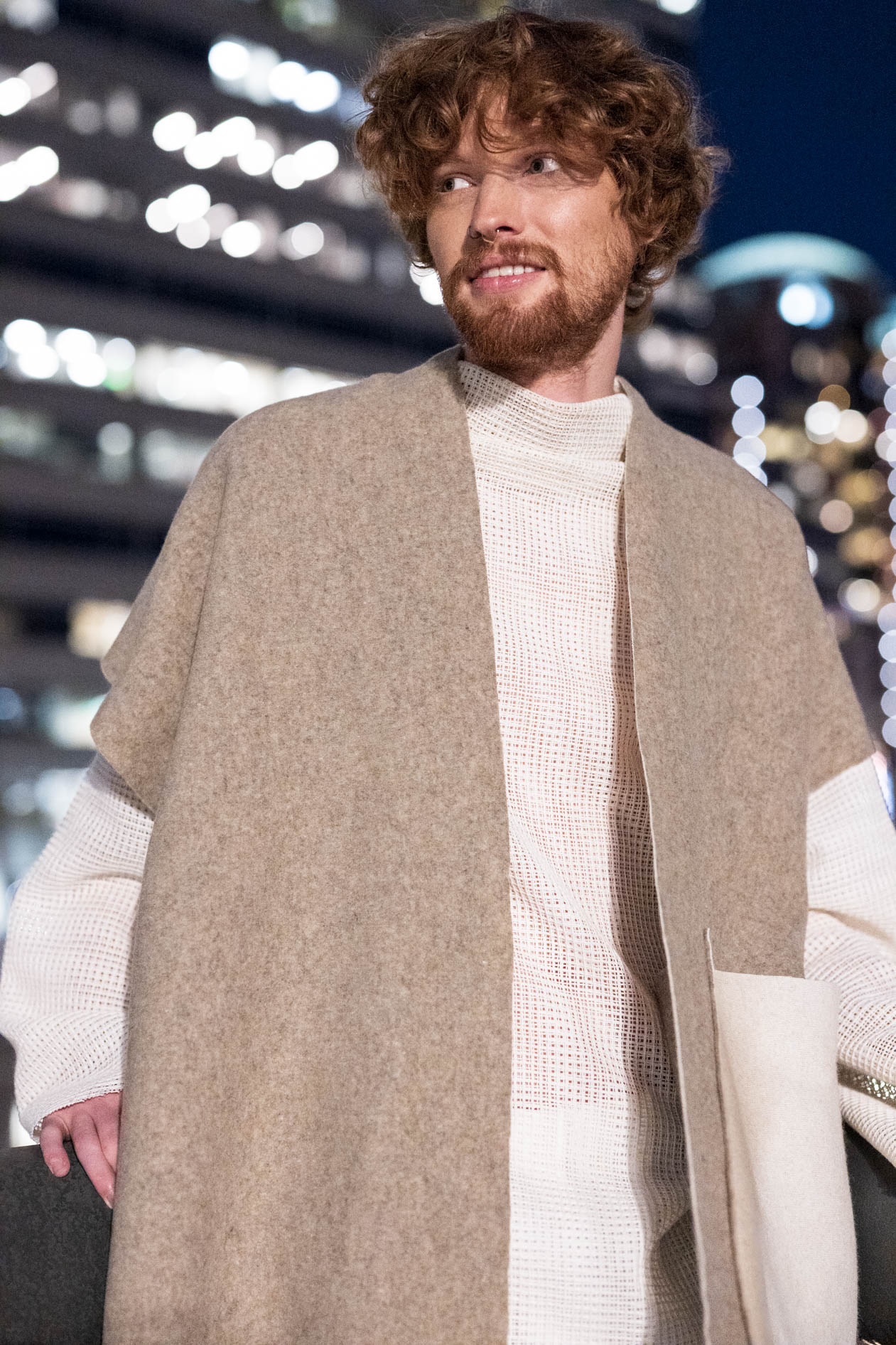 A commercial portrait of a male model with reddish hair and a beard, wearing a beige poncho over a white knit shirt from the boutique brand Ale O. This image showcases lifestyle brand photography in Portland, Oregon.