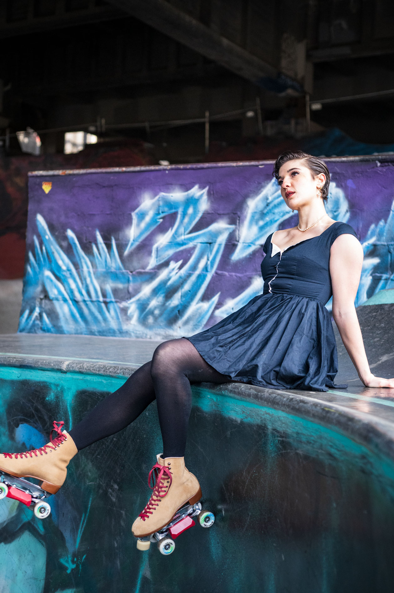 An inclusive portrait of a nonbinary model, Ana Gonzalez, wearing a dress and roller skates, sitting in a skate park in Portland, Oregon.