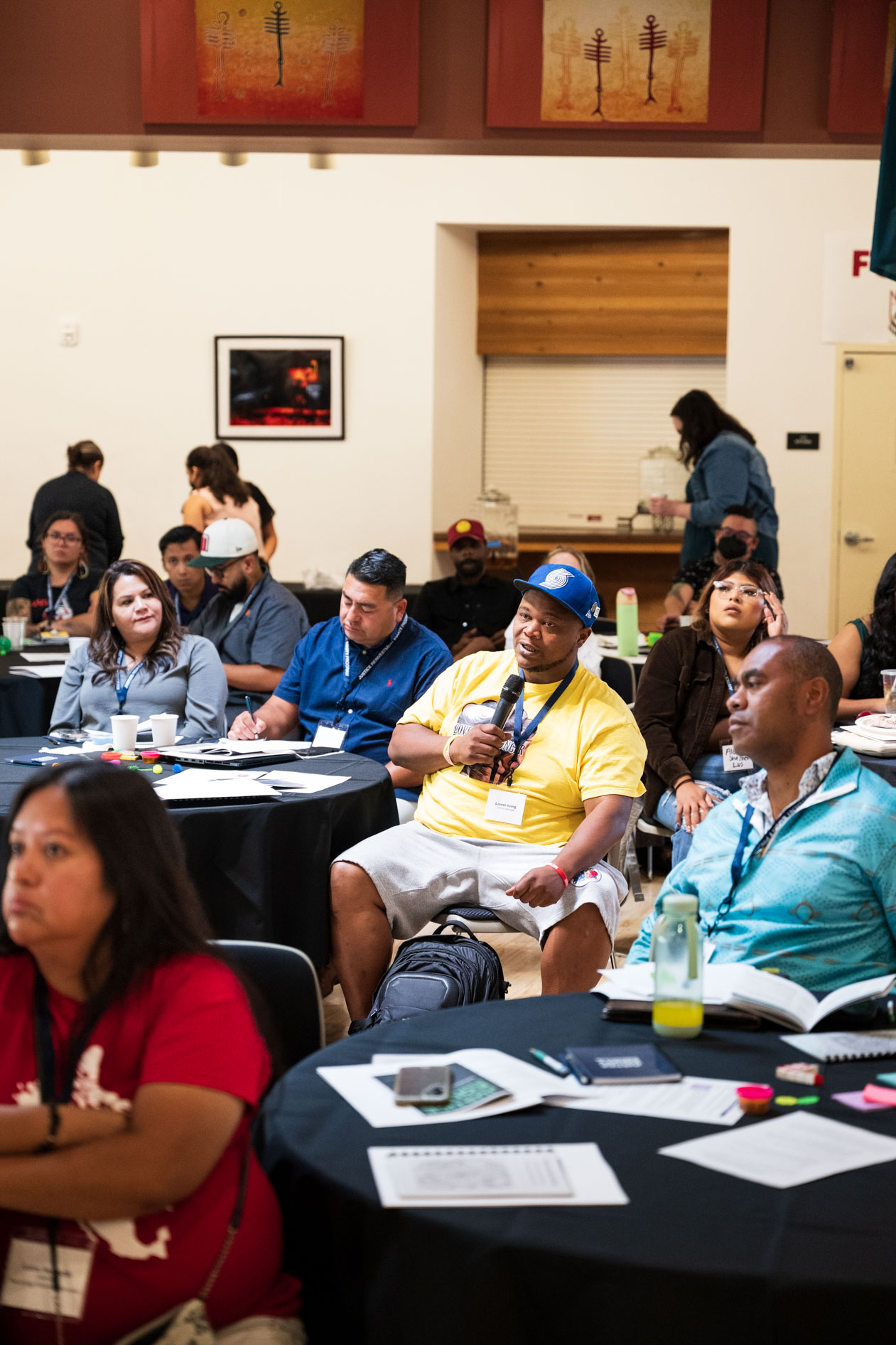 A candid photograph of a JREP grantee speaking into a microphone while seated at a table during the Northwest Health Foundation convening event.
