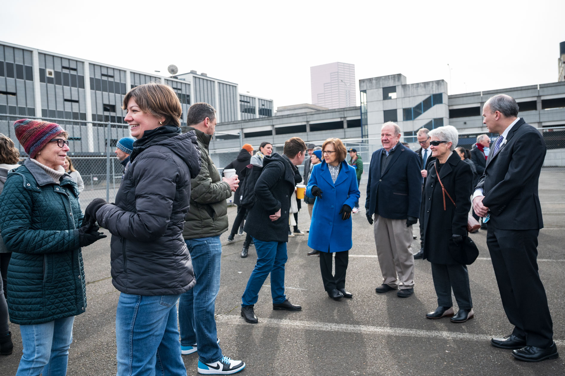 A candid photograph of elected officials and attendees socializing before the demolition event, with the Portland skyline in the background. This showcases corporate event photography.