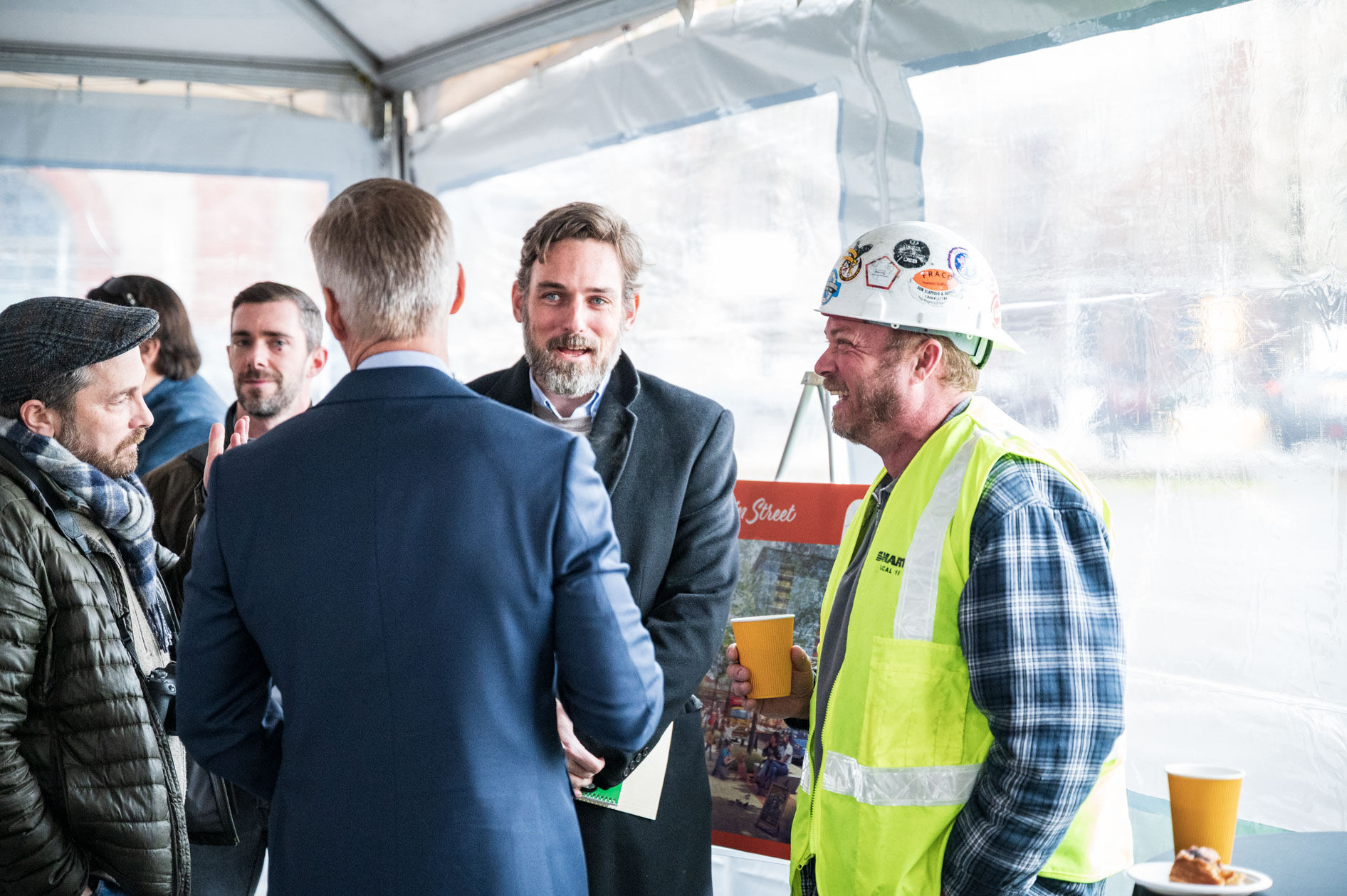 A candid photograph of Prosper Portland attendees, including officials and a construction worker in a safety vest, networking at the downtown demolition event.