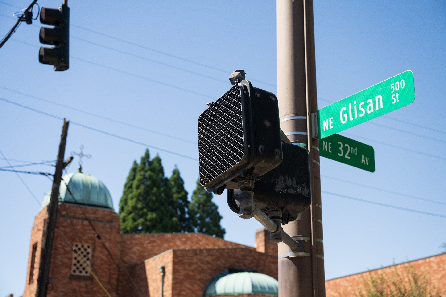 A street sign reading NE Glisan St and NE 32nd Ave in Portland, Oregon, with a brick church building in the background.