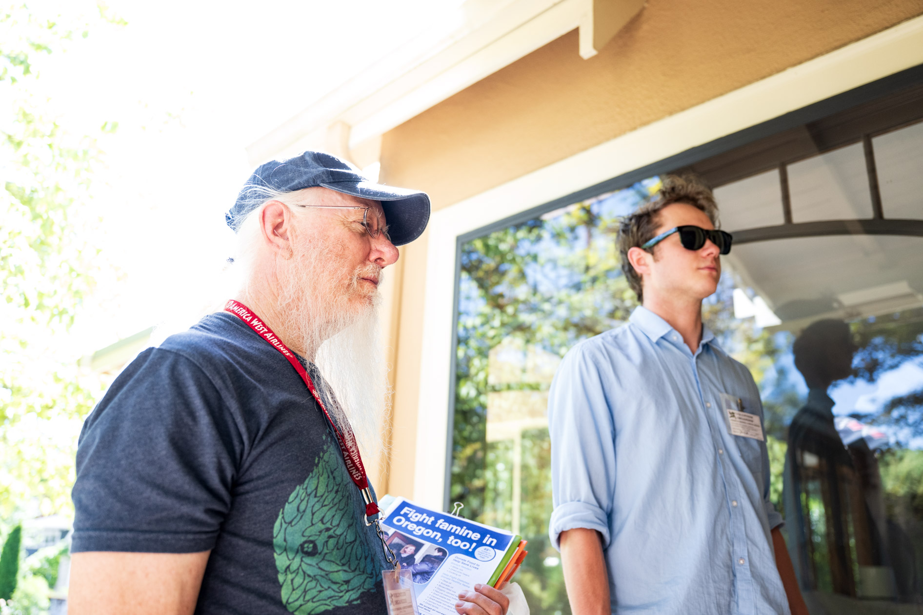 Two volunteers for Friends of Seasonal and Service Workers (FSSW) stand on a porch, holding informational flyers while canvassing for a food drive.