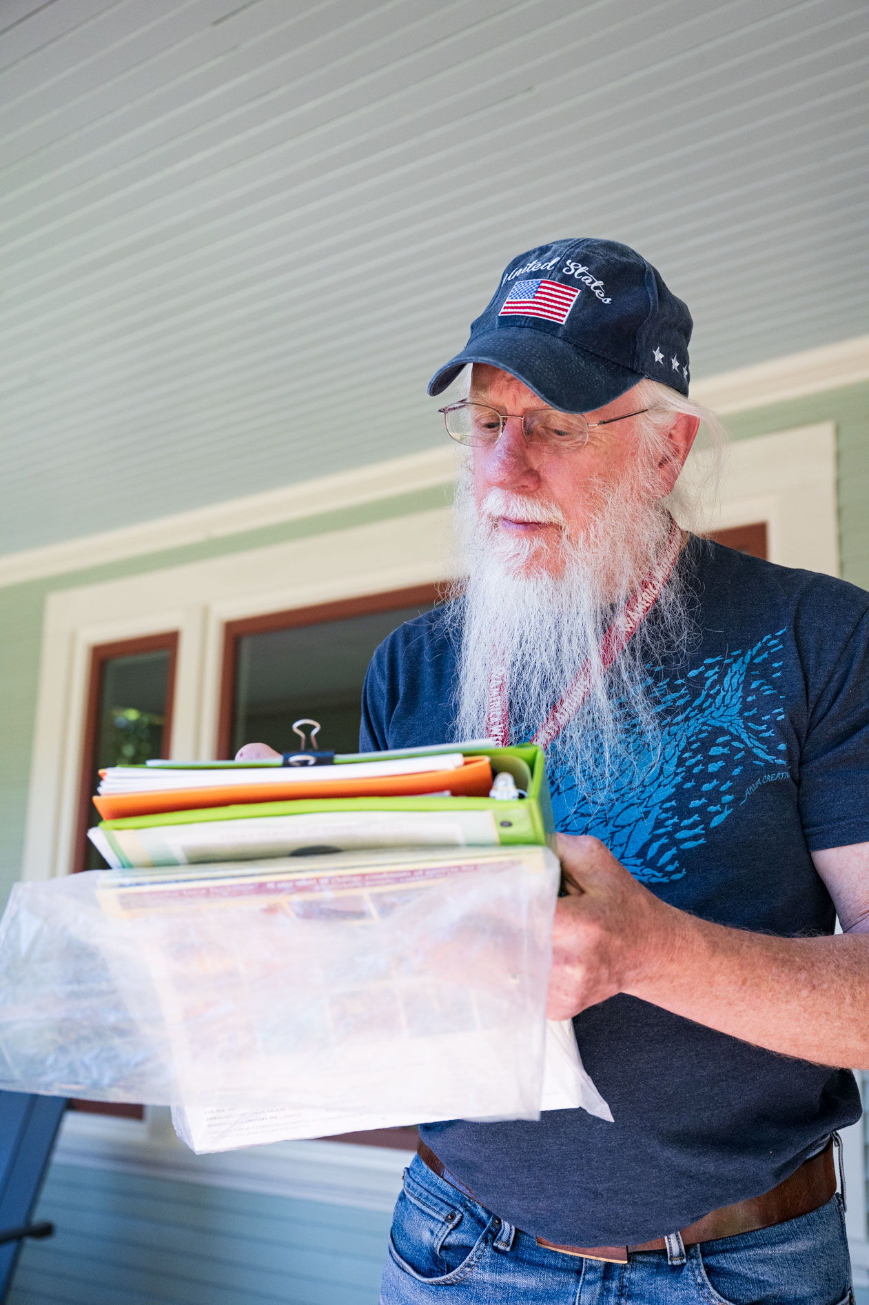 An authentic portrait of a long-bearded FSSW volunteer wearing an American flag hat, holding flyers while canvassing for a food drive.