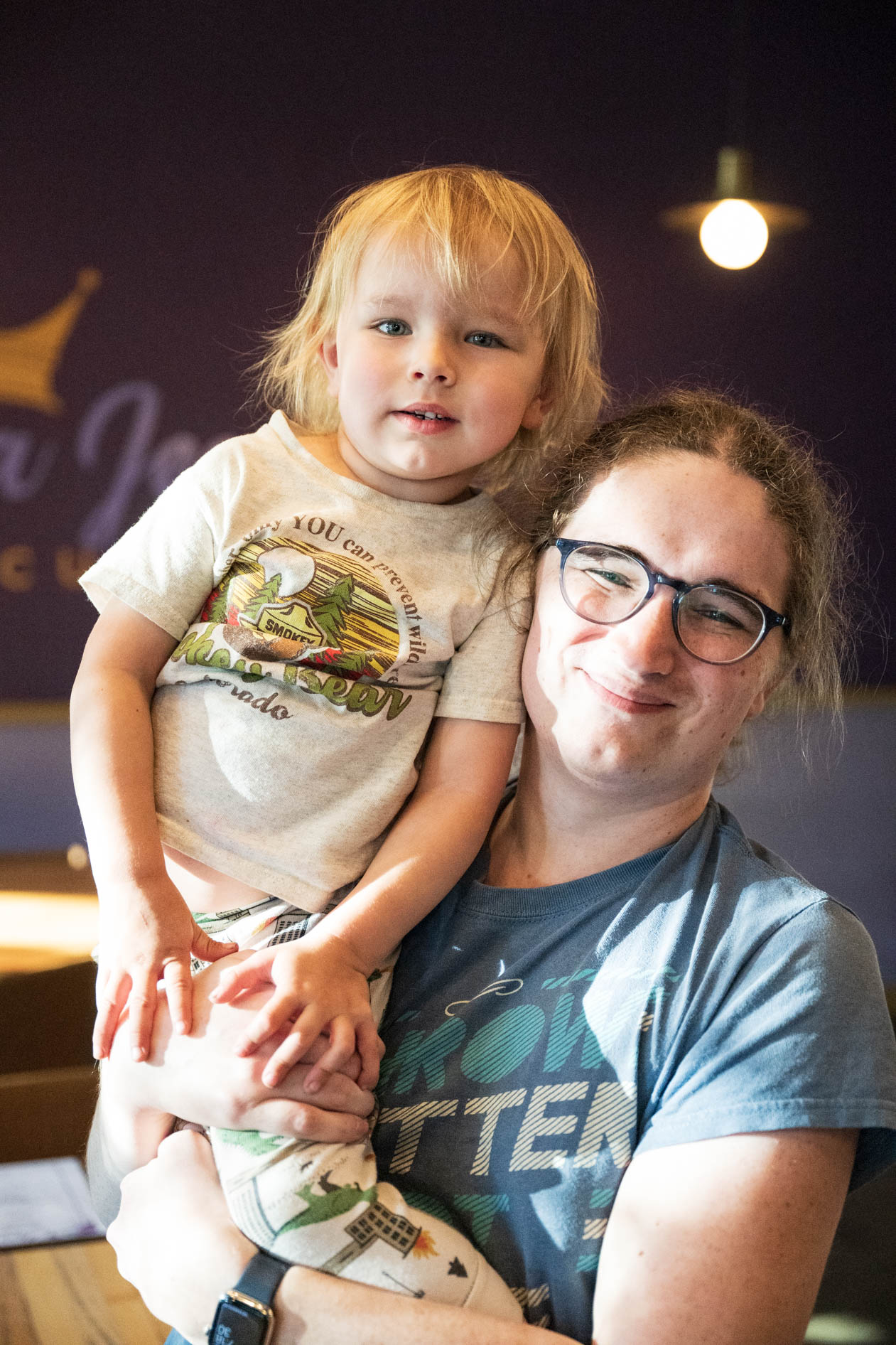 A candid portrait of a parent holding their smiling child, inside a restaurant. This showcases commercial photography and brand storytelling for Norma Jean's Soul Cuisine in NE Portland.