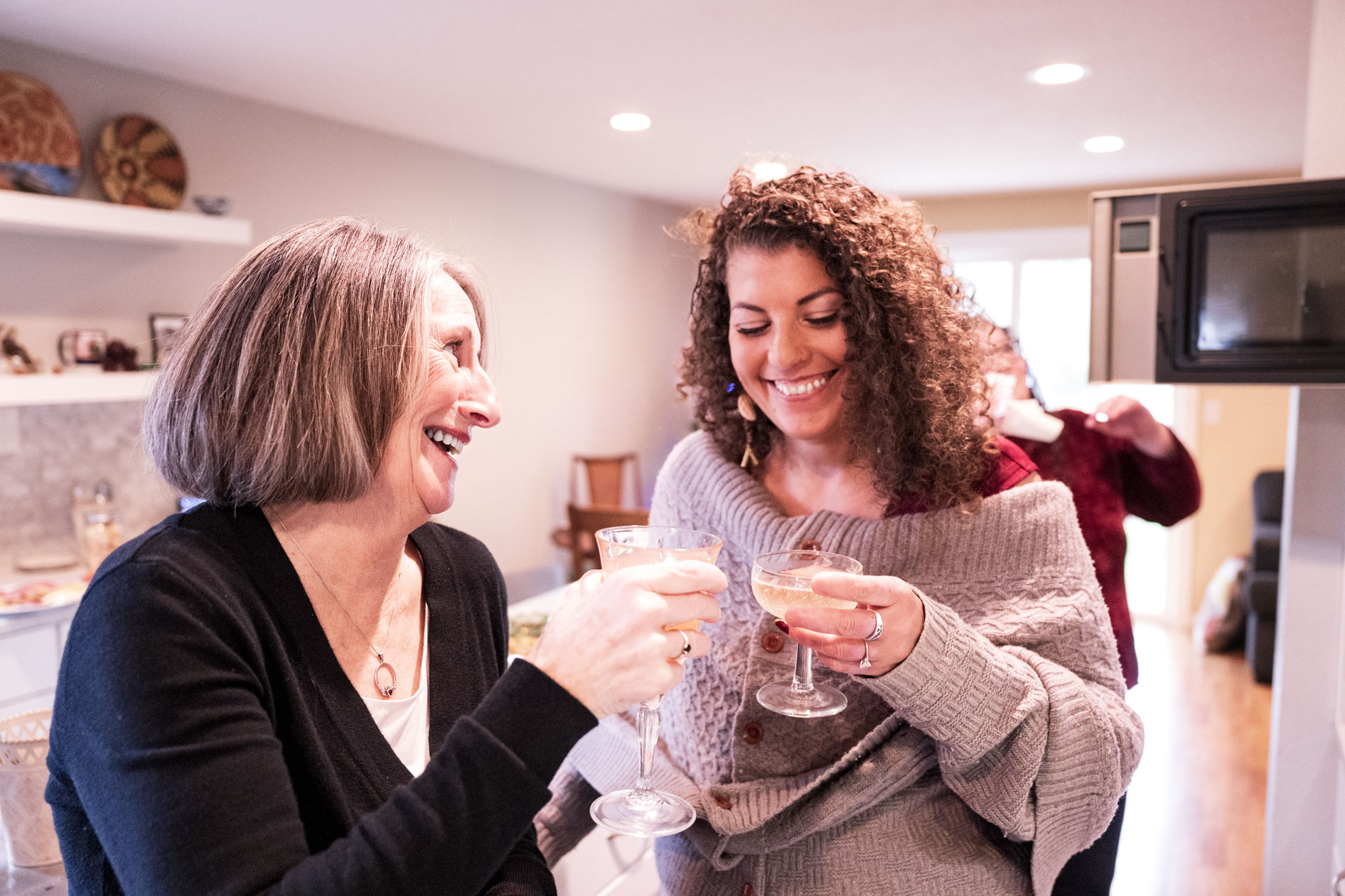 A candid portrait of two people smiling and toasting with champagne glasses in a kitchen during a holiday family photography session in Beaverton, Oregon.