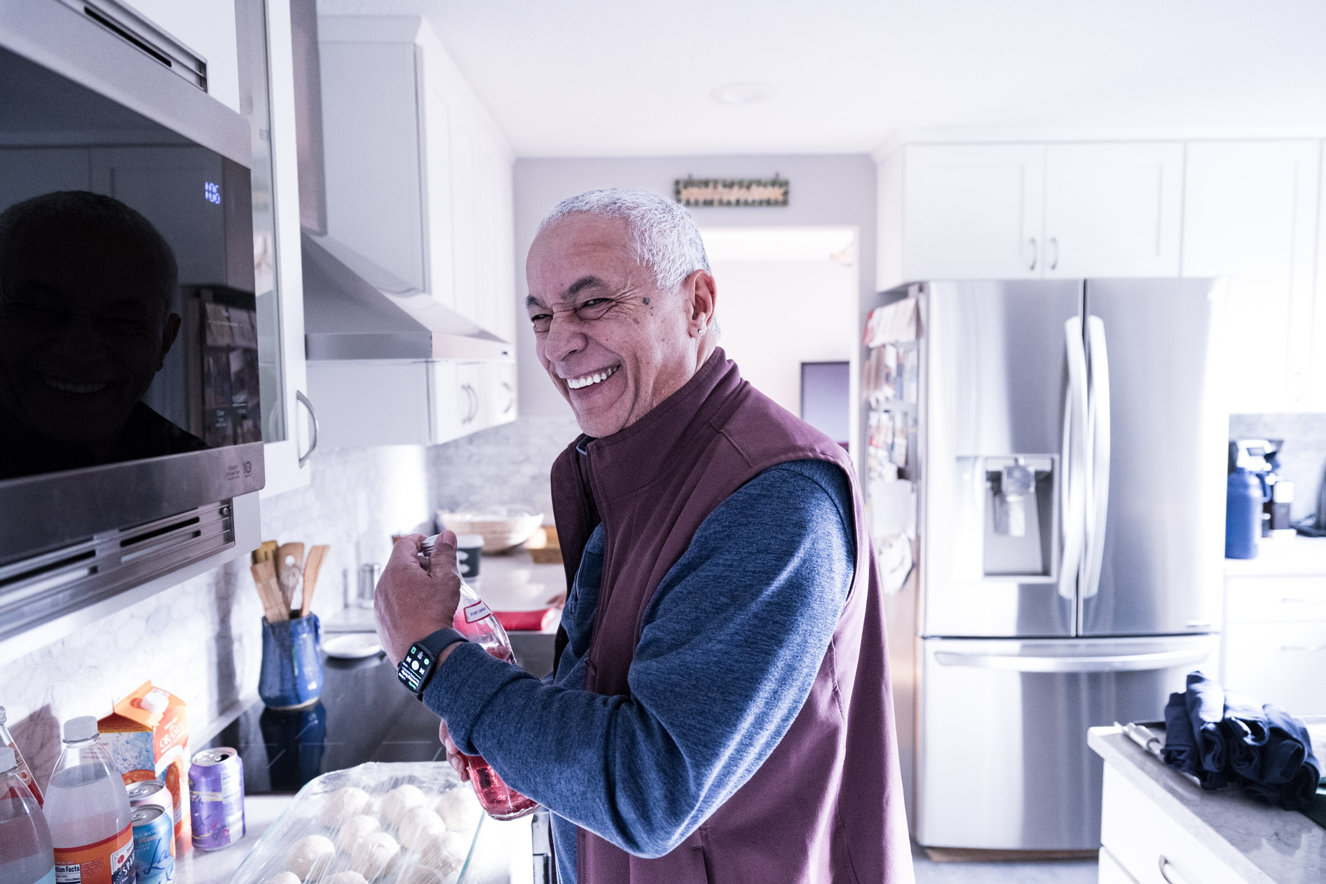 A candid, joyful inclusive family portrait of a person laughing while preparing drinks in a bright kitchen during a holiday session in Beaverton, Oregon.