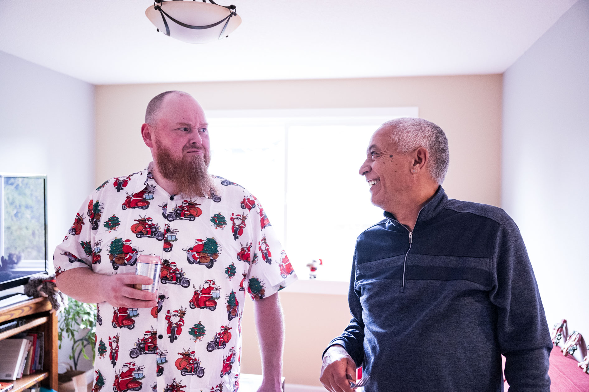 A candid portrait of two people talking and laughing indoors. One person wears a festive holiday shirt. This showcases inclusive family photography in Beaverton, Oregon.