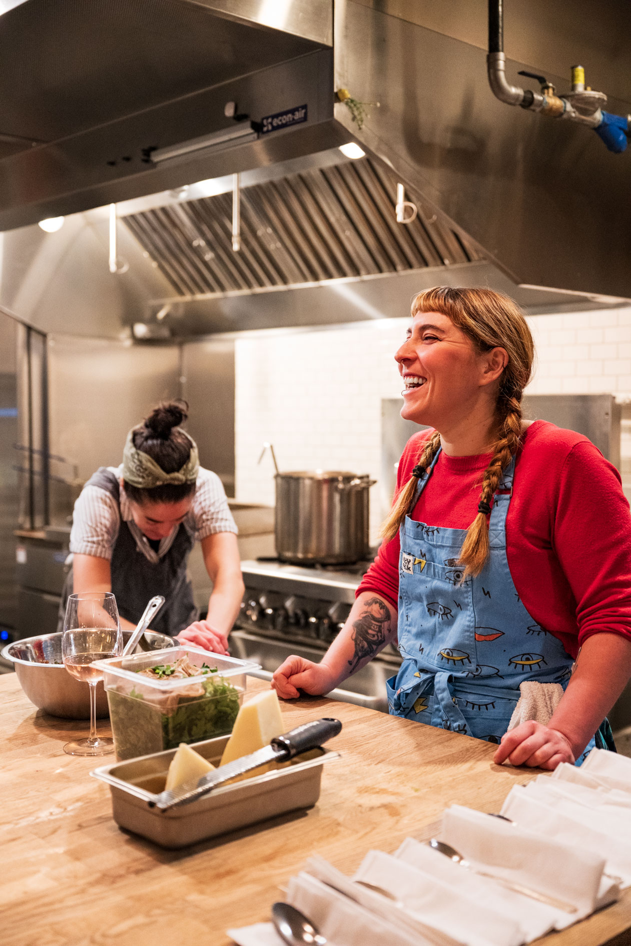 Candid documentary photography of two kitchen volunteers laughing together at Che during Soup Night, a community fundraiser in Northeast Portland.