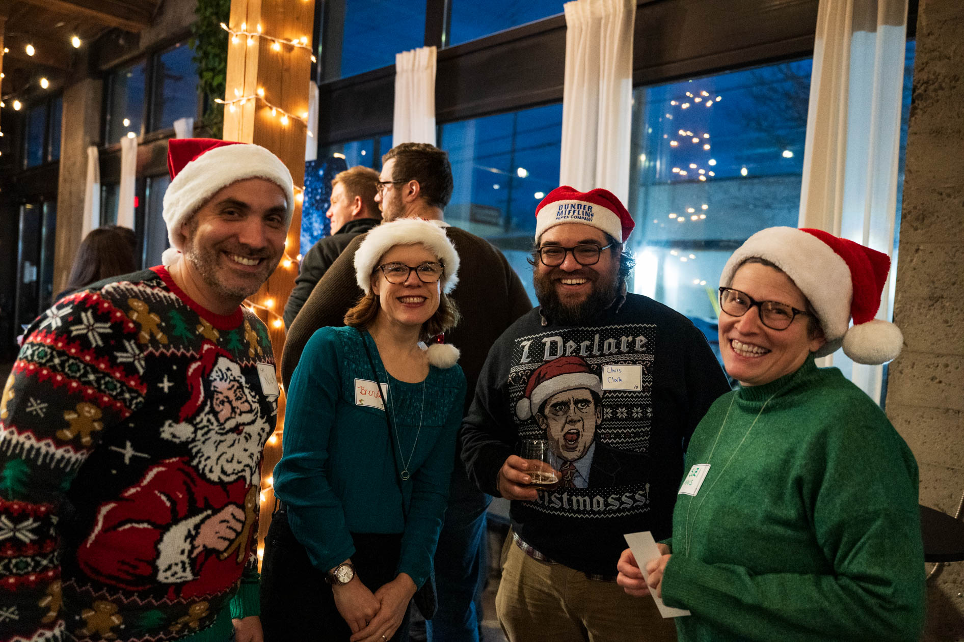 Four people smiling and wearing Santa hats and festive holiday sweaters while posing together at a party in Portland.