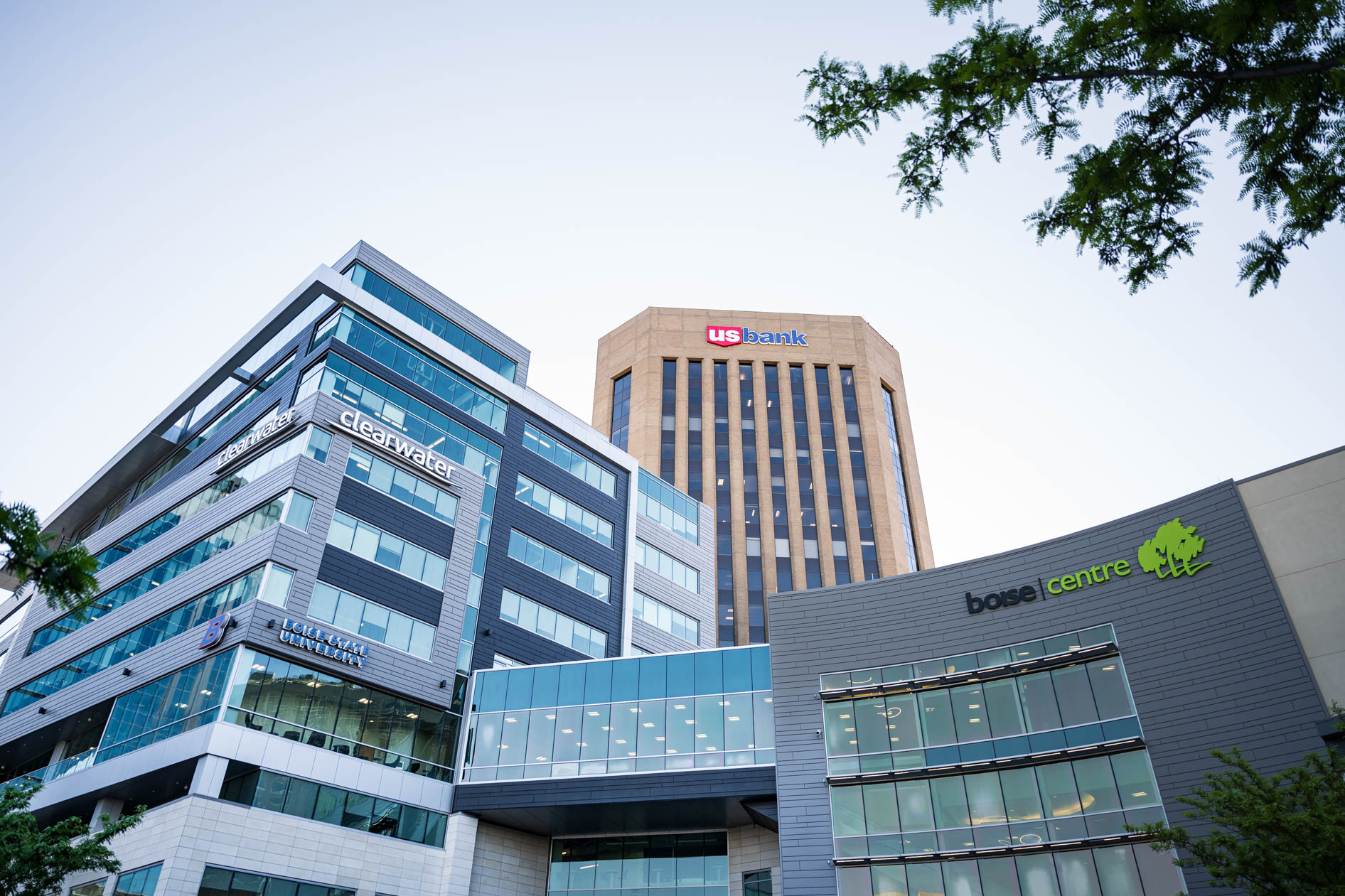 A low-angle exterior shot of the Boise Centre convention building, venue for the Efficiency Exchange 2026 conference. The modern complex is surrounded by downtown buildings, including the Clearwater and U.S. Bank towers under a clear sky.