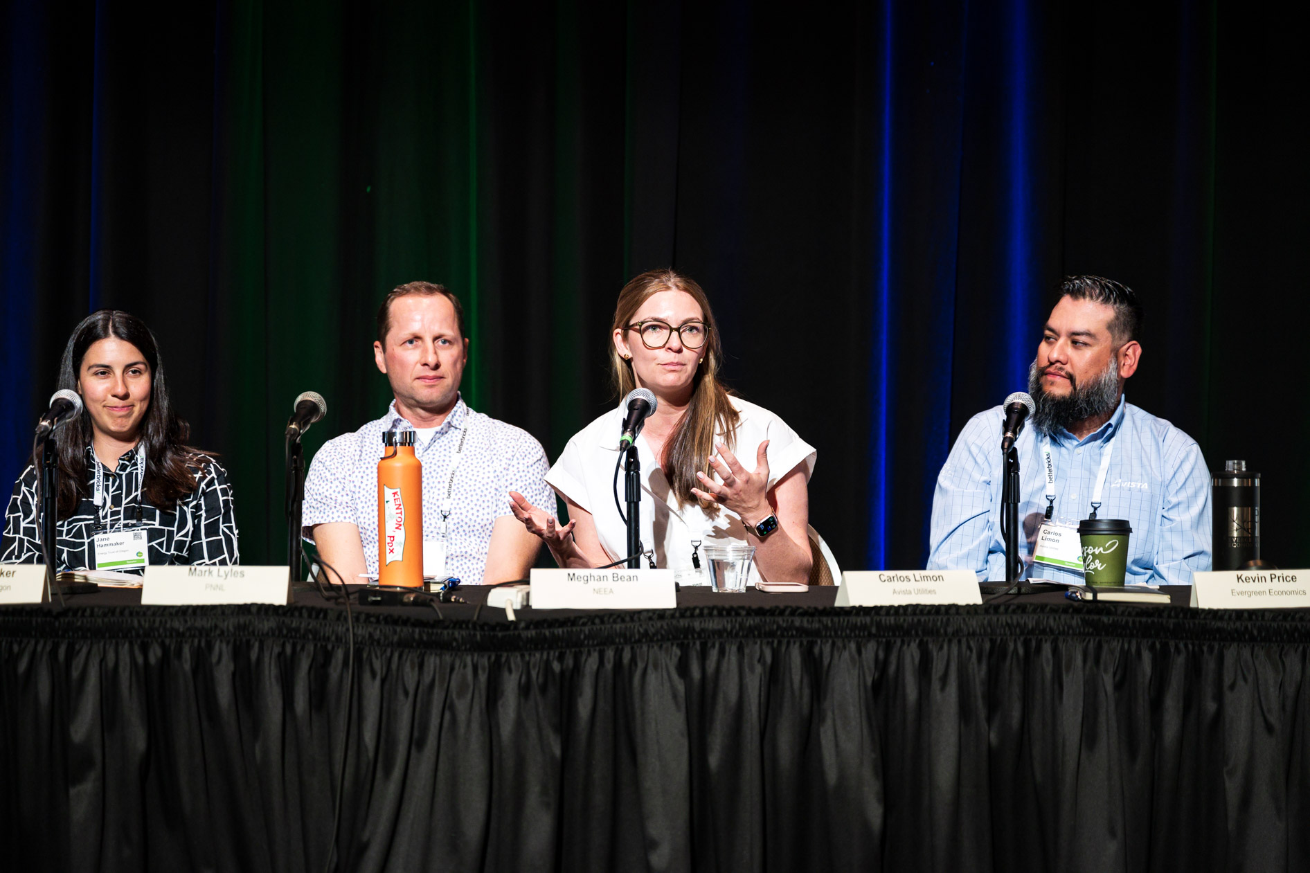 Four panelists sit at a long table during a discussion at the Efficiency Exchange 2026 conference. A woman with glasses speaks into a microphone while the other three panelists look on against a dark stage curtain.