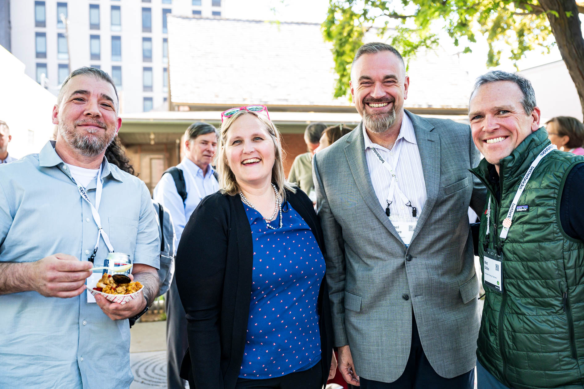 Four smiling attendees pose together outdoors during a reception at the Efficiency Exchange 2026 conference. They wear event lanyards and casual business attire, with one person holding a small plate of food.