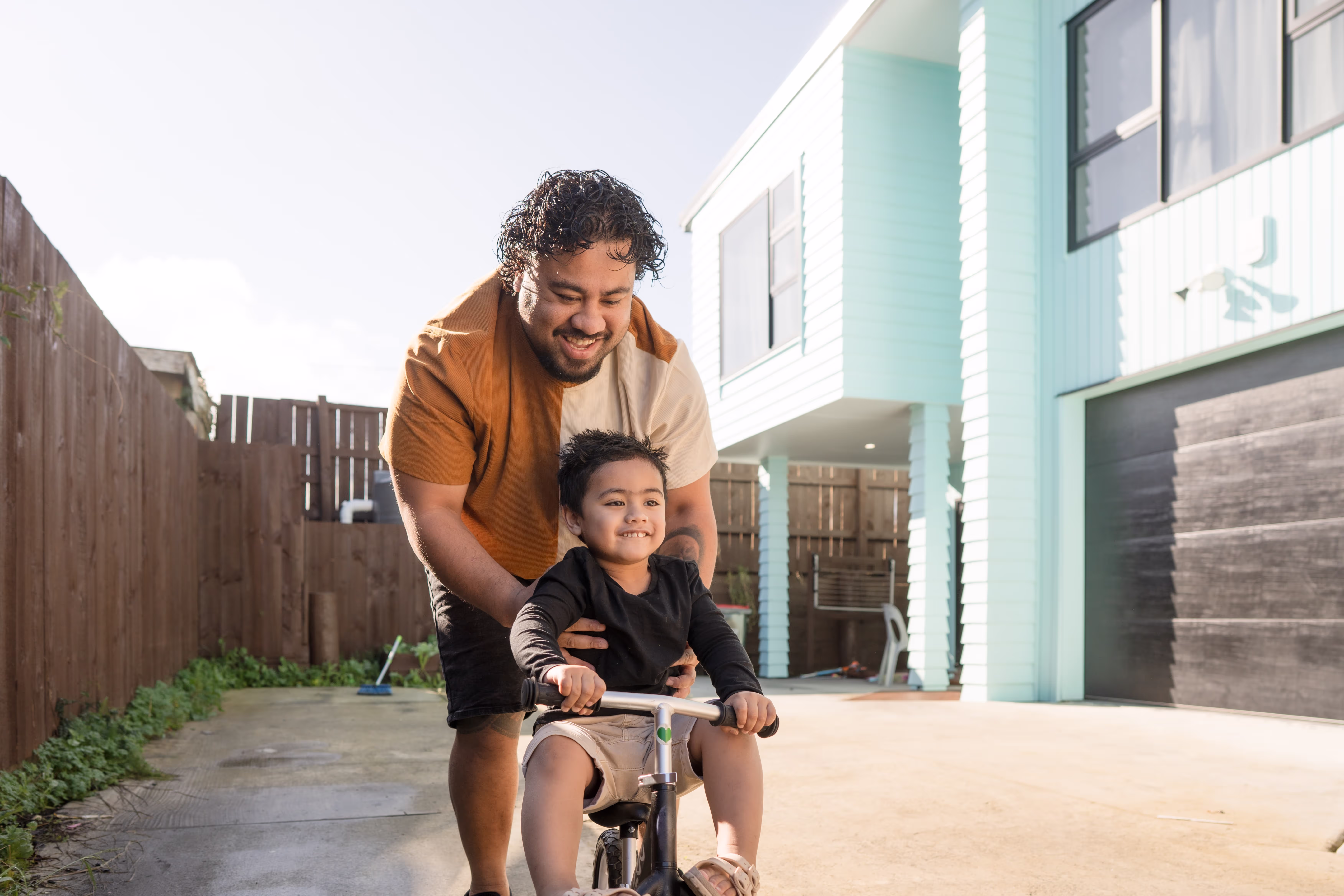 A man and a child are riding a bike in front of a blue house.