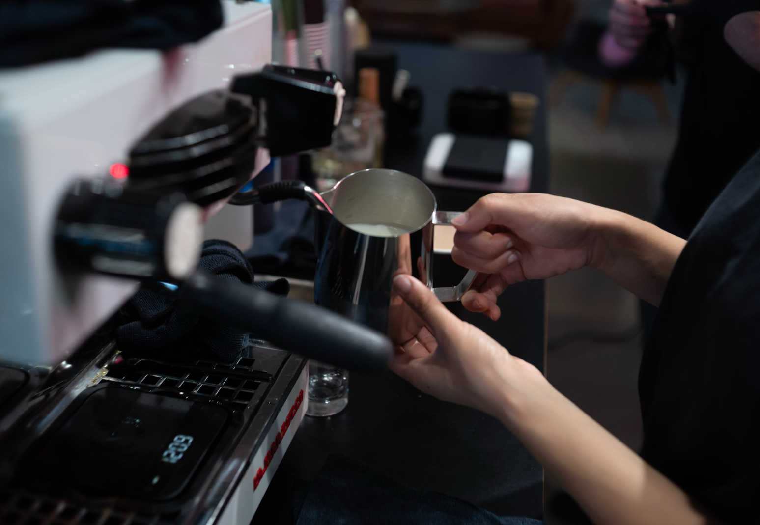 A barista steaming milk in a pitcher with an espresso machine.