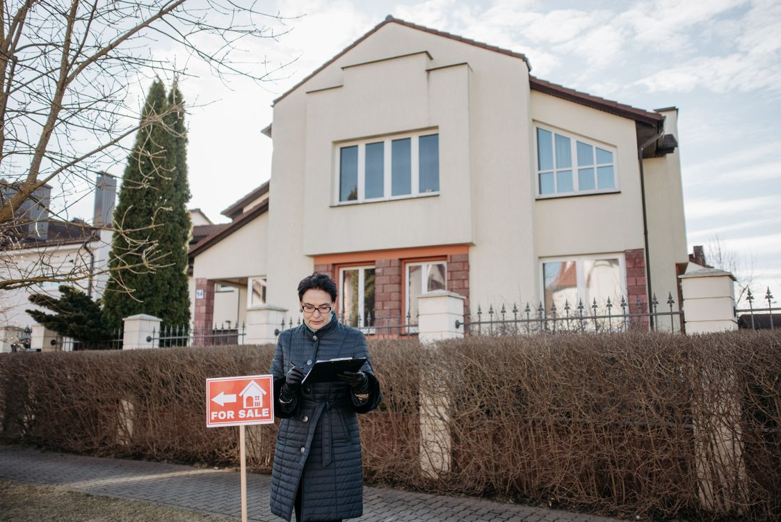 woman in jacket standing by house for sale