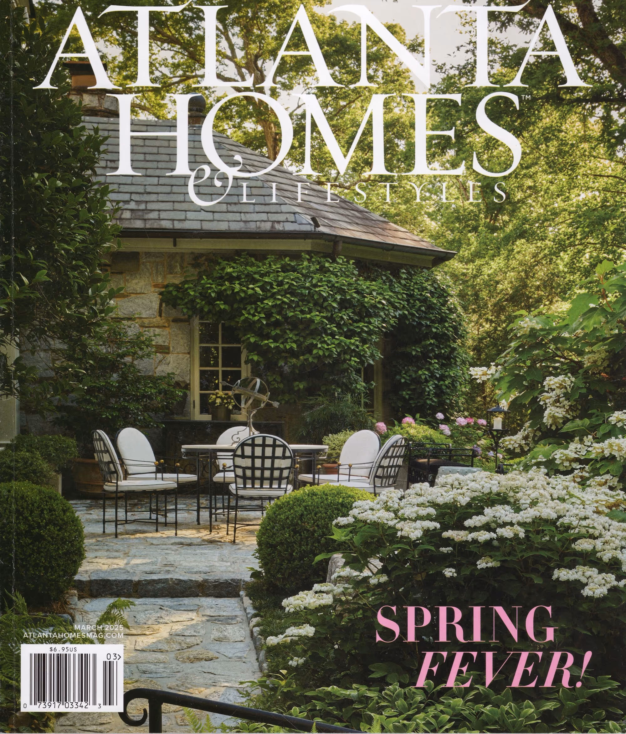 The March 2025 cover of Atlanta Homes & Lifestyles features a lush garden terrace with stone paving, classic black-and-white dining chairs, and blooming spring greenery surrounding an ivy-covered home.