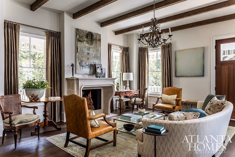 A refined living room from the 2024 Serenbe Showhouse, featuring exposed beams, layered antiques, tailored upholstery, and a soft-hued Moattar rug grounding the collected, artful space.