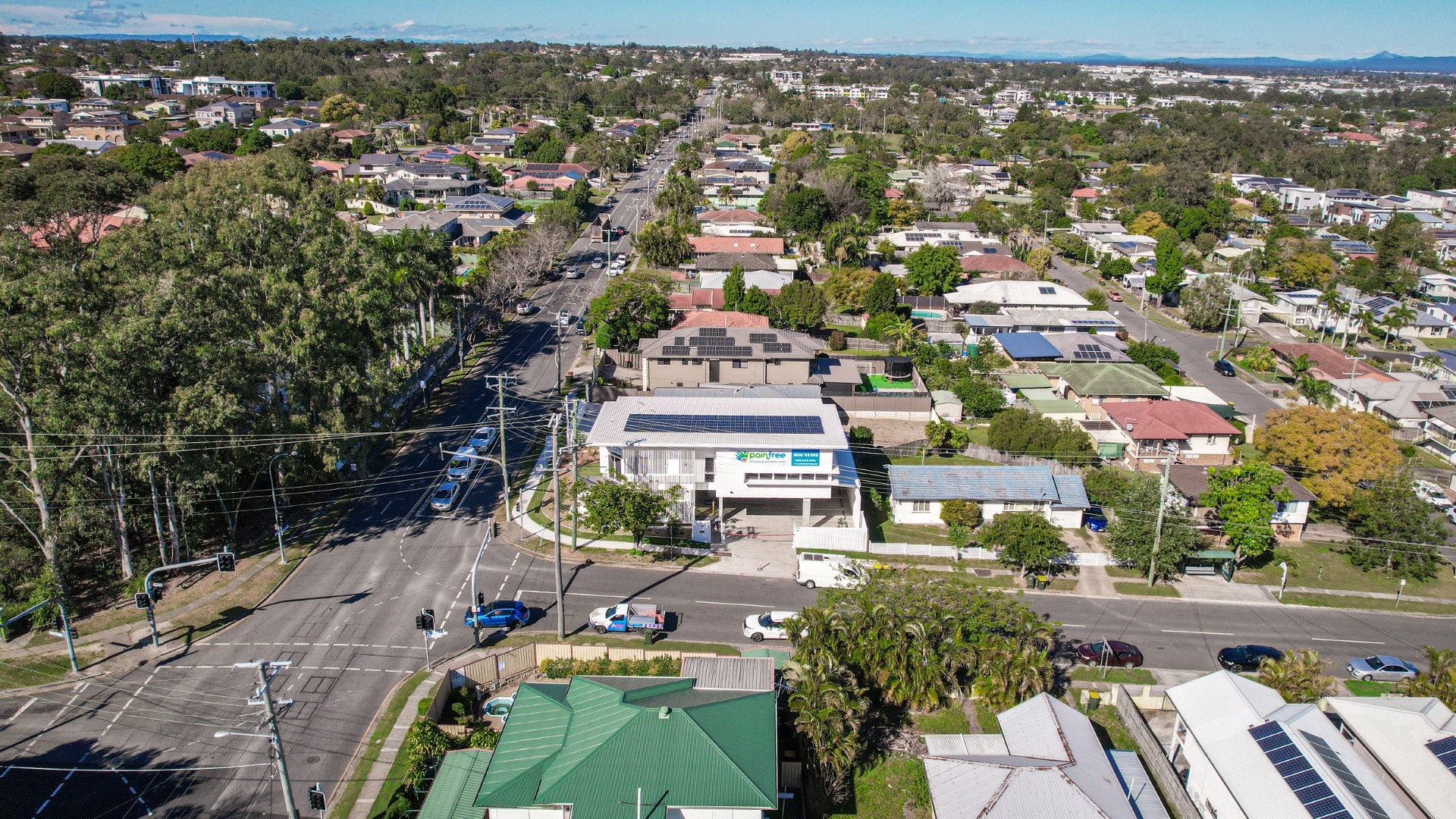 Aerial view of a suburban neighborhood with houses, streets, trees, and solar panels on some roofs on a clear day.