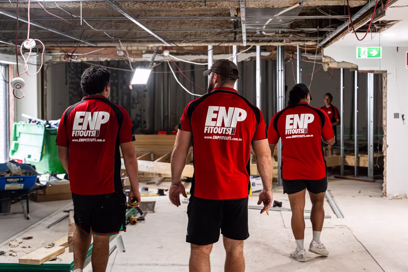 Three workers wearing red ENP Fitouts shirts standing in a partially constructed interior space with exposed ceiling and framing.