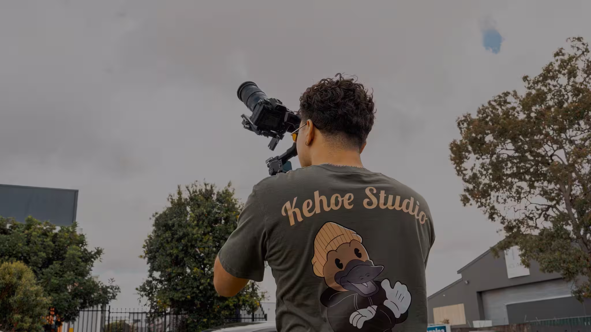 Photographer wearing a Kehoe Studio shirt captures an outdoor scene with a large camera rig.