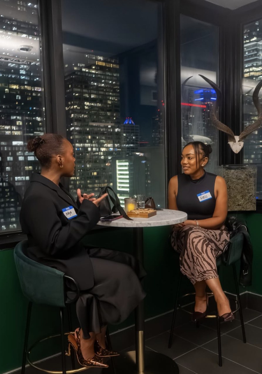 Two guests talking at a high-top table overlooking the city skyline at a hotel speakeasy