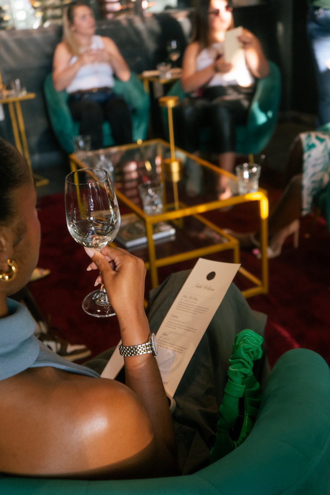 Guest holding a wine glass and tasting menu in a lounge during a community wine tasting