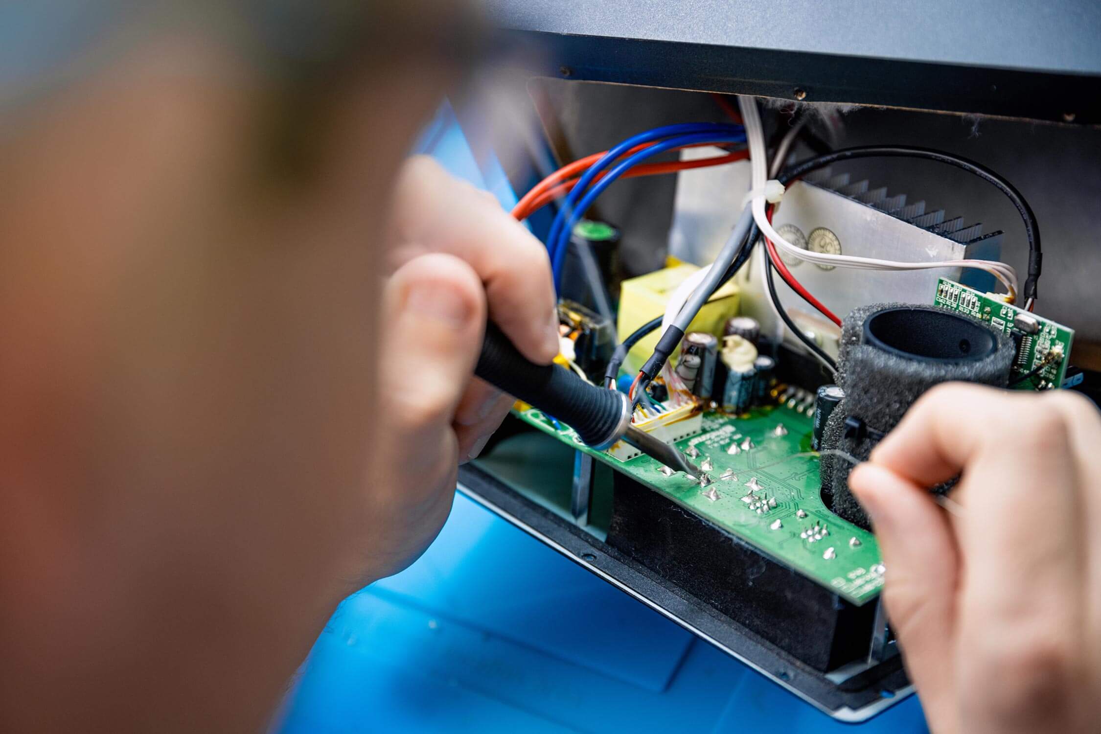 A technician solders wires onto a circuit board inside an open device.