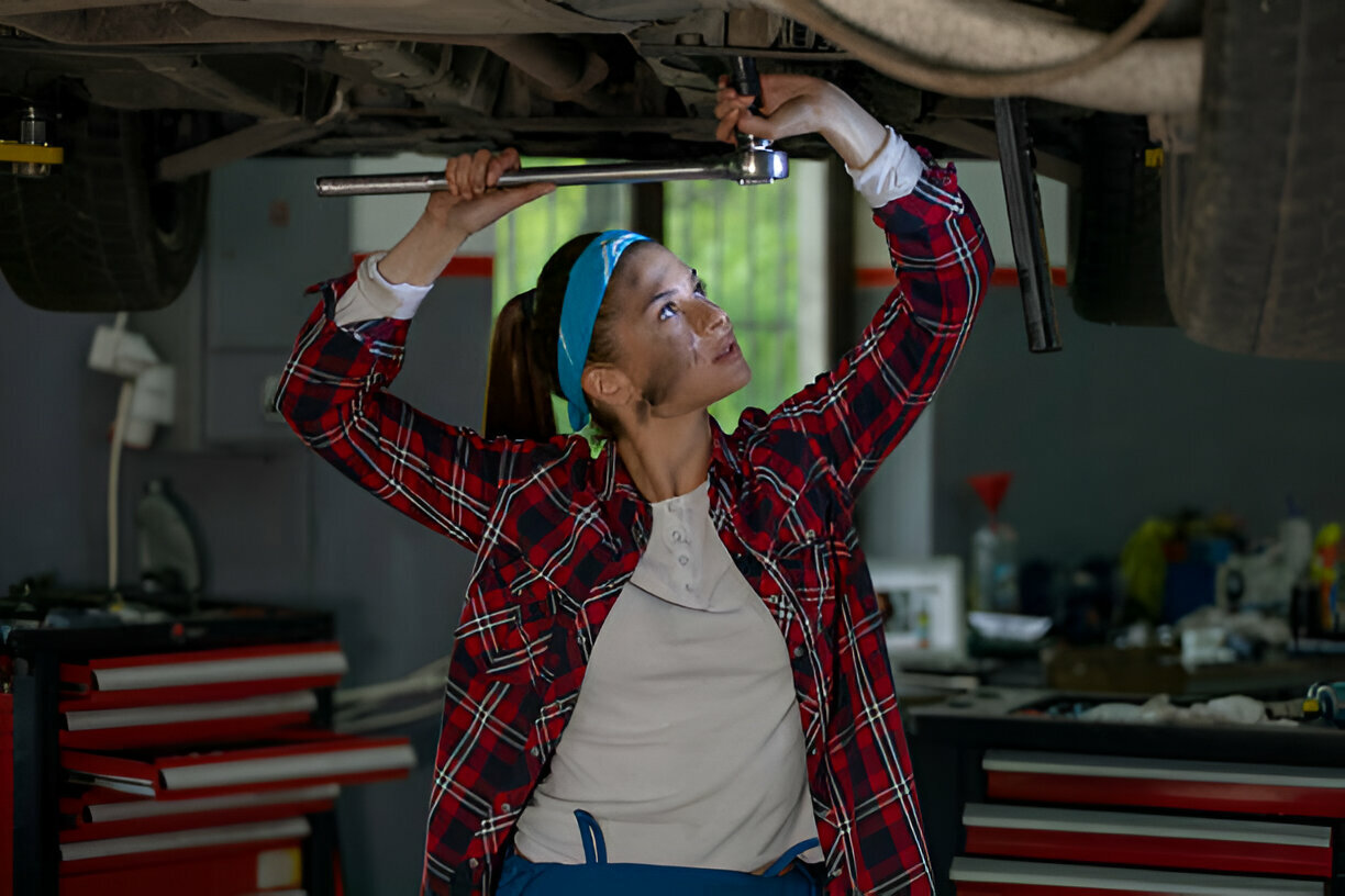 Woman mechanic working under car using wrench in auto repair shop