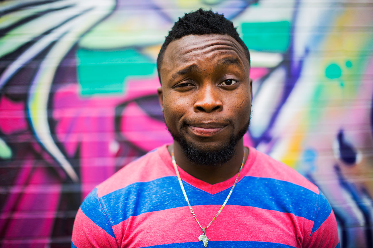 Person in striped shirt standing in front of colorful graffiti wall