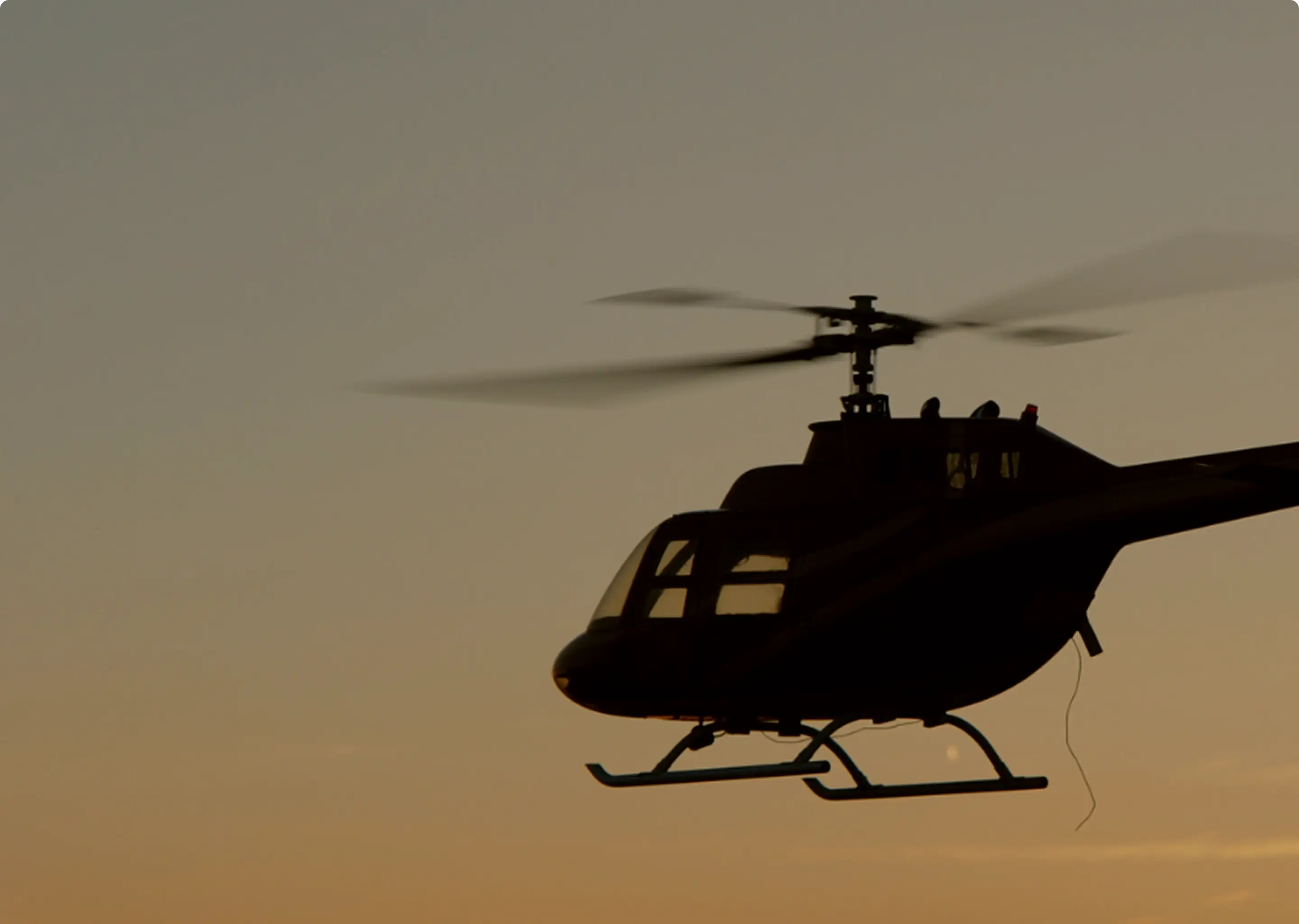 Silhouette of a helicopter flying against a golden sunset sky