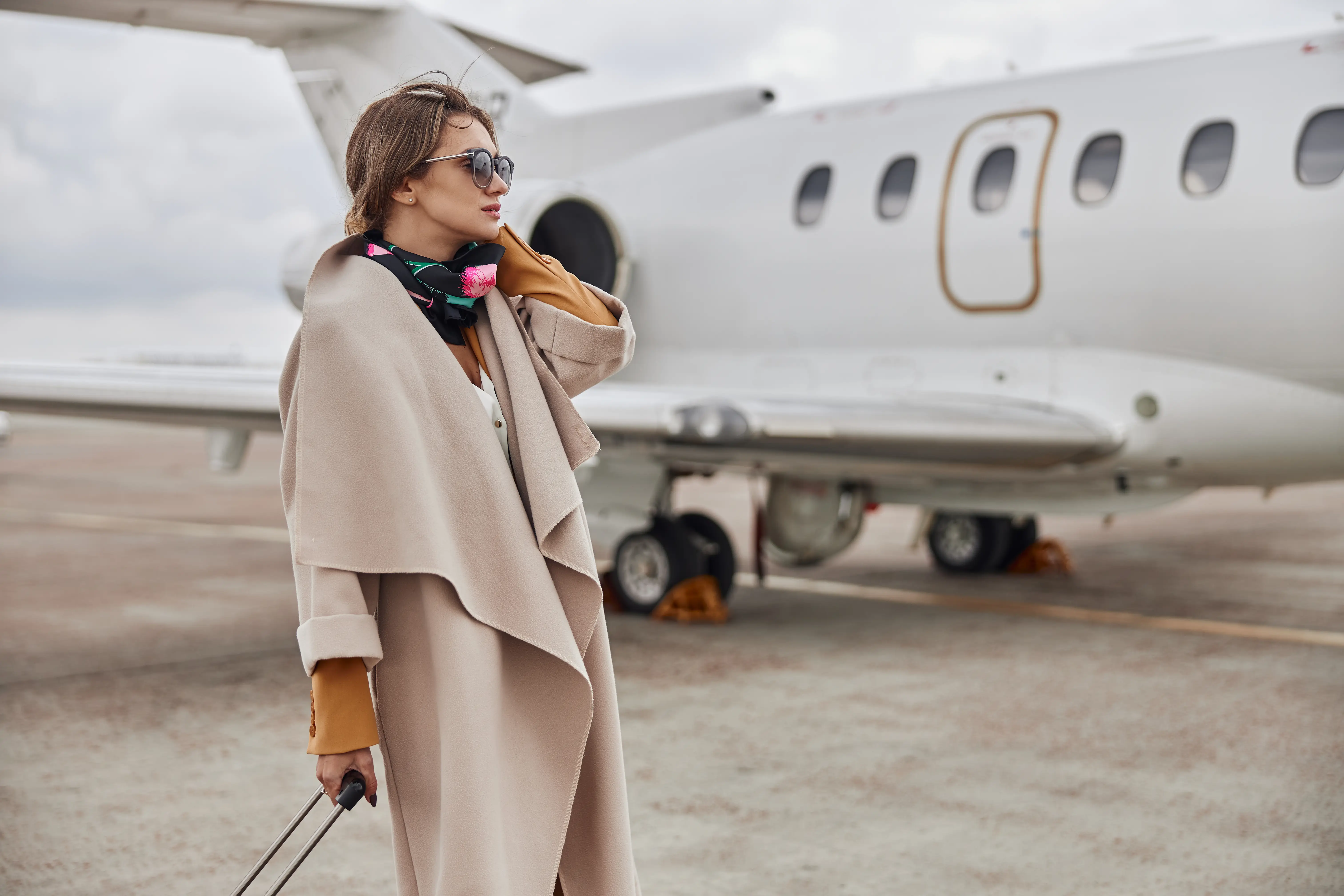 Stylish traveler with sunglasses standing near private jet on runway