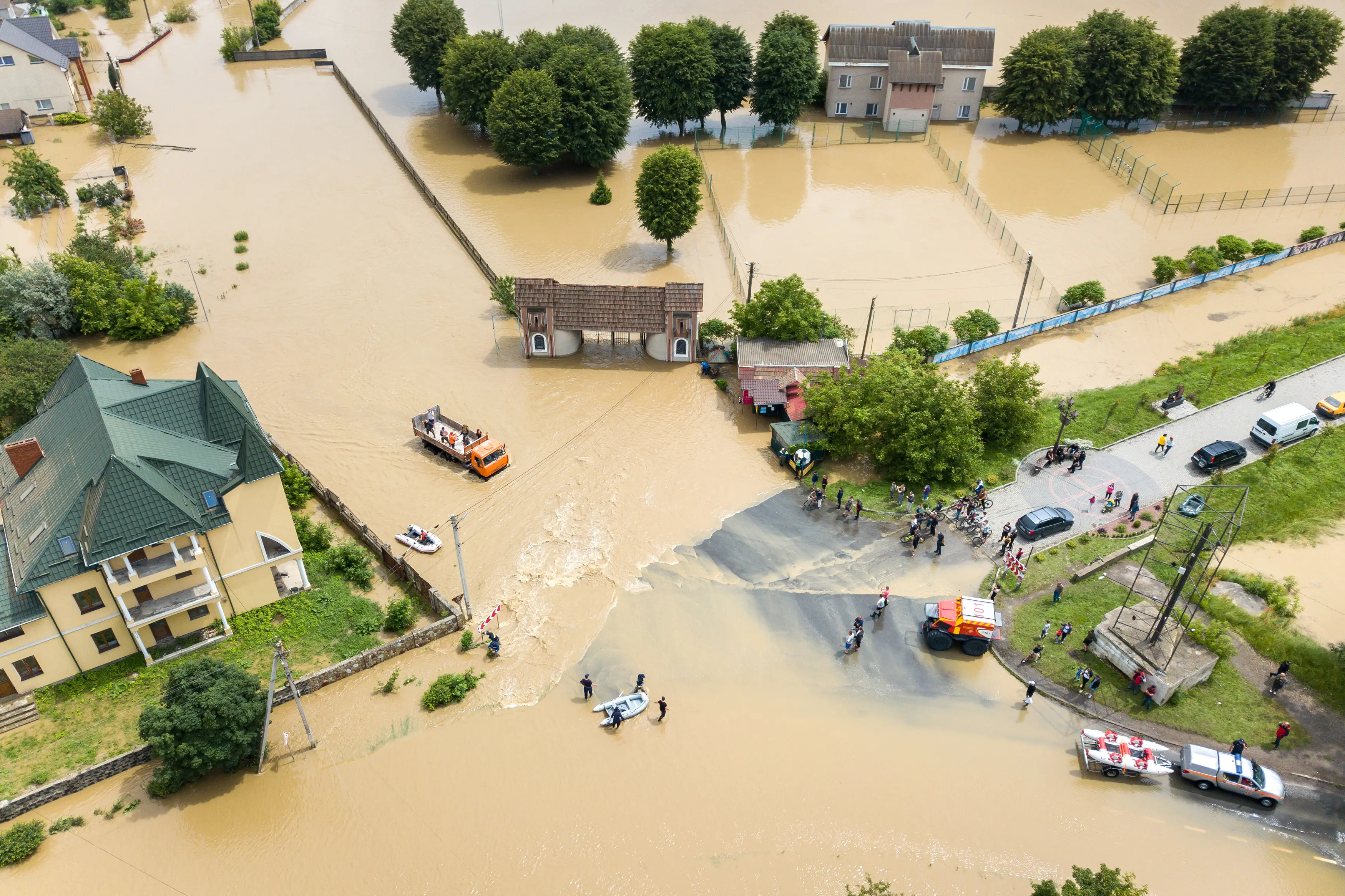 Aerial view of severe flooding, rescue vehicles and people navigating muddy waters