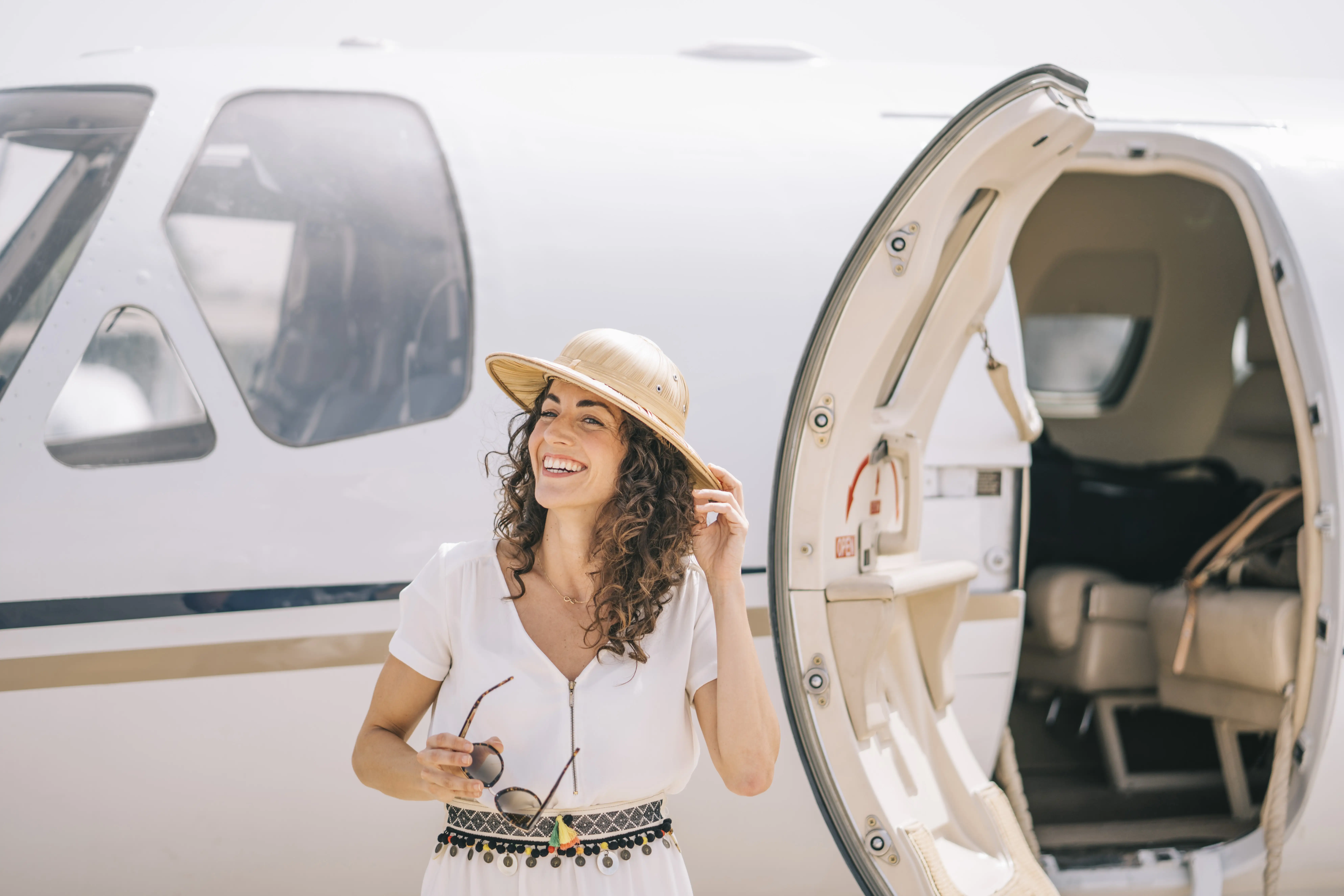 Smiling woman in sun hat standing next to small aircraft door