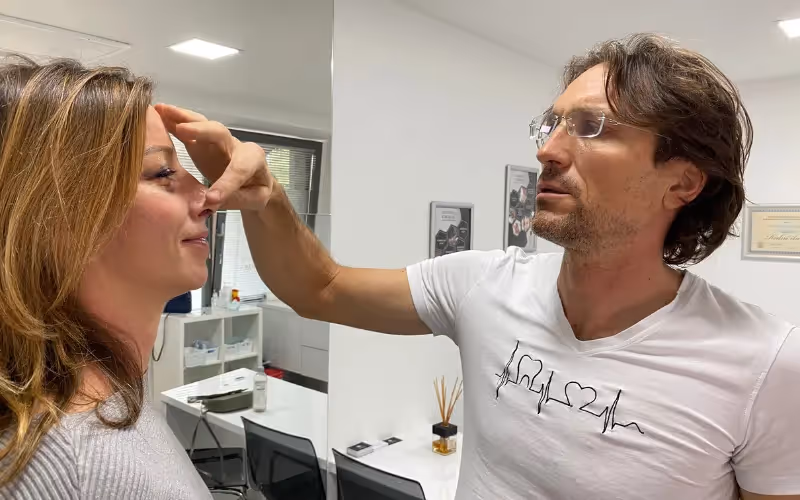 Kirurg Matic Fabjan med posvetom za rinoplastiko pregleduje nos ženske v srednjih letih.
