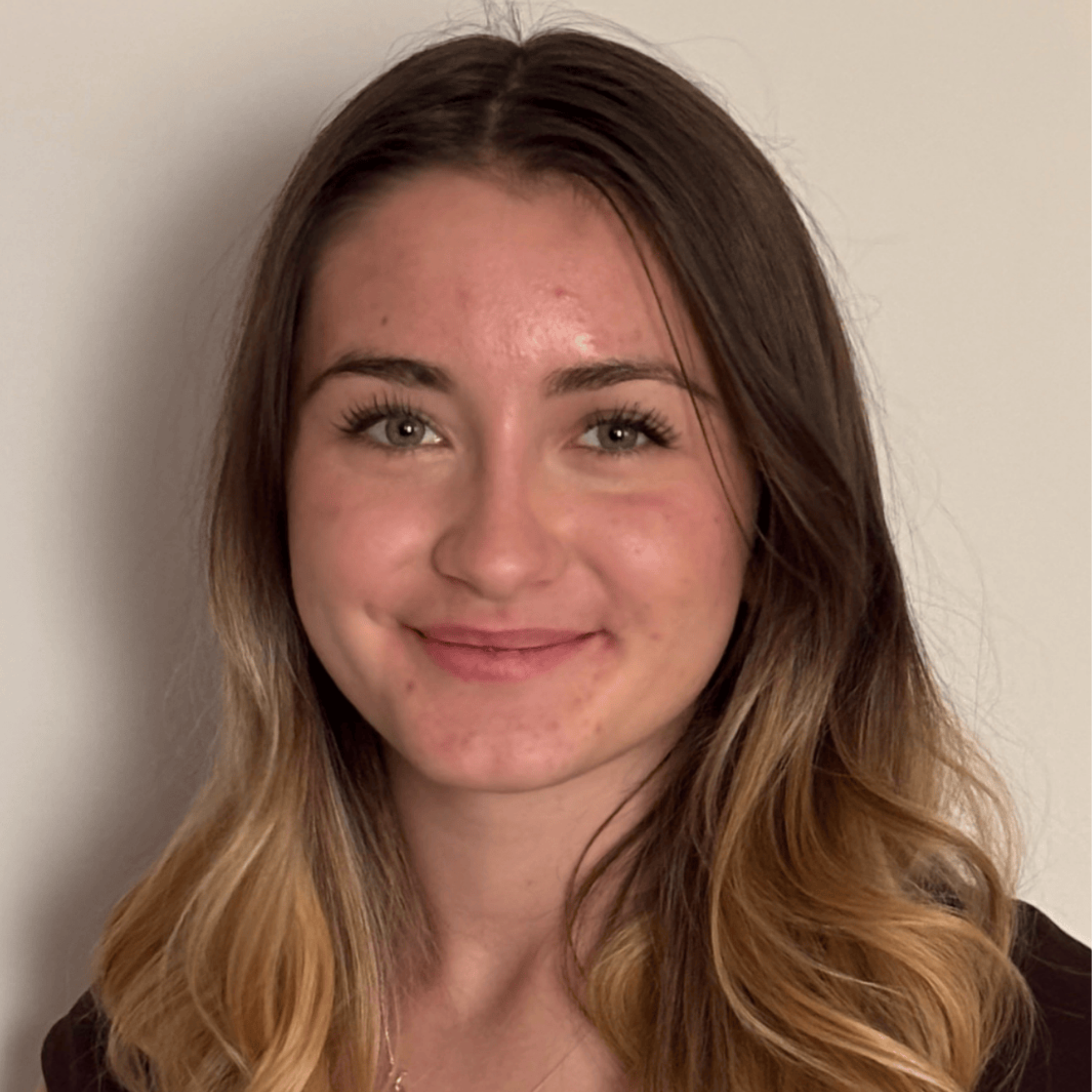 Smiling young woman with long brown and blonde hair against a plain light background.