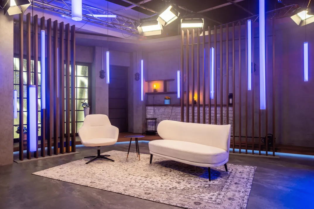 Modernes Wohnzimmer mit weißem Sessel, Sofa, kleinem runden Tisch und blau leuchtenden Pendelleuchten.