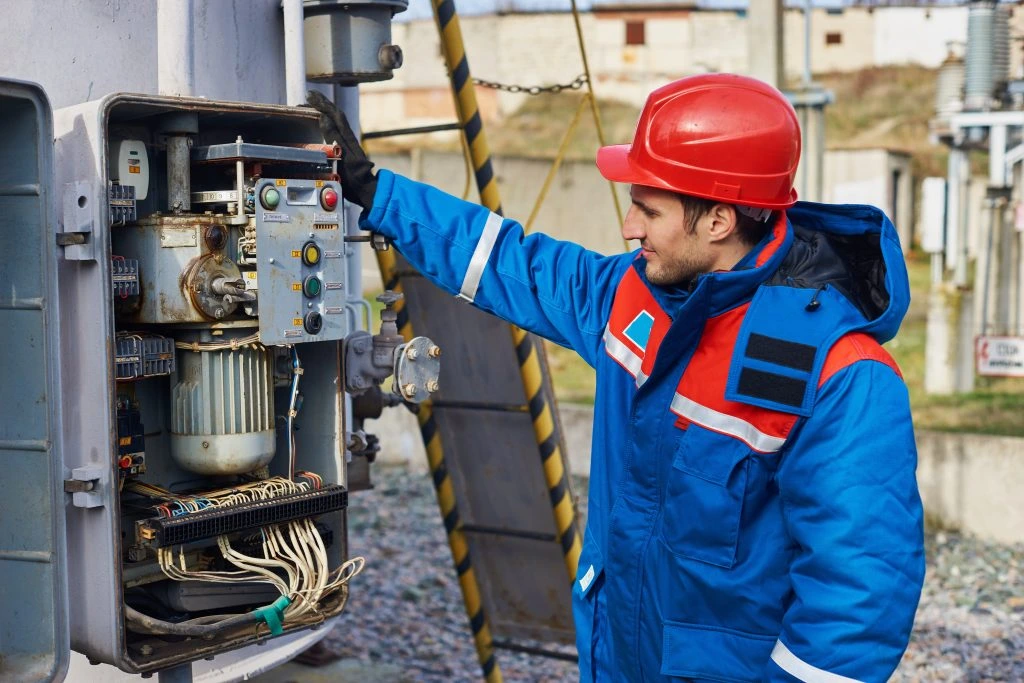 Electrical worker in red hard hat checks industrial control panel outdoors