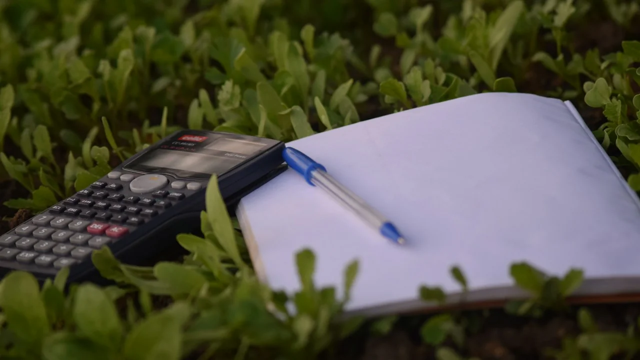 Rekenmachine, pen en open boek op een groene ondergrond