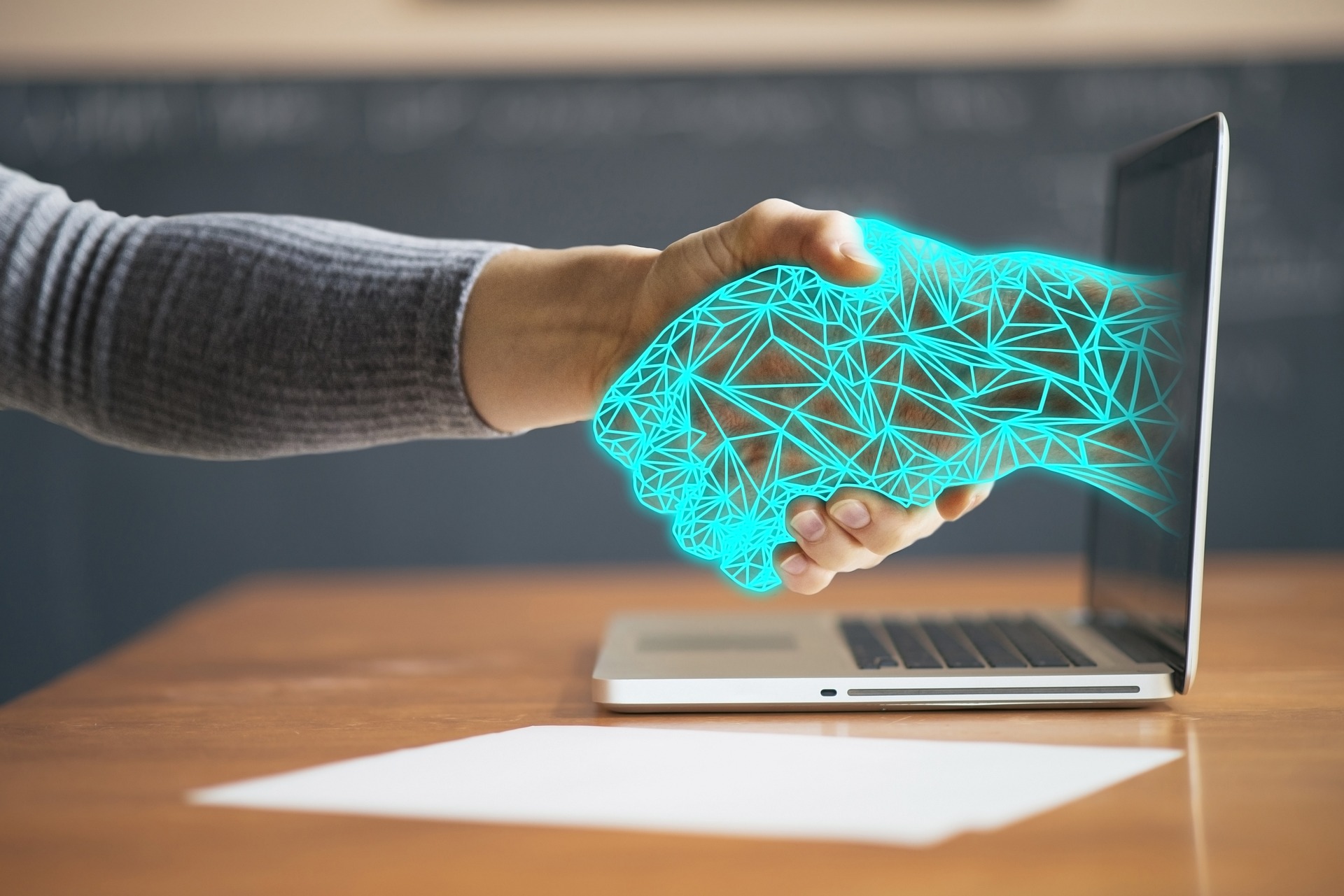 Image of a human hand holding a virtual hand that is coming from the laptop screen