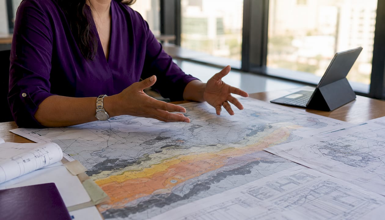 Hands pointing at shale formation map and blueprints