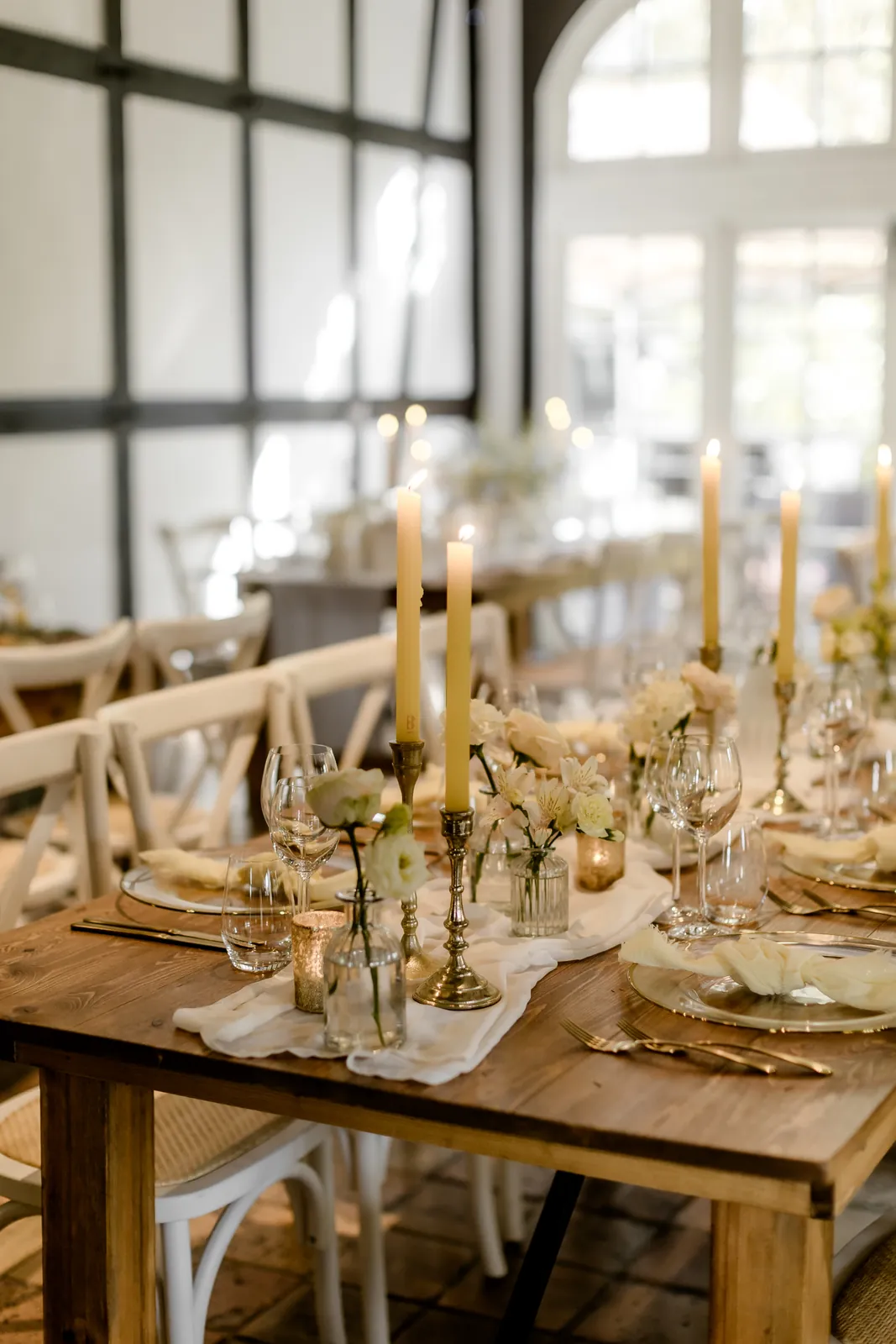 Lange Hochzeitstafel von PURE FLAIR mit goldenen Kerzenleuchtern und weißer Floristik vor Sprossenfenster