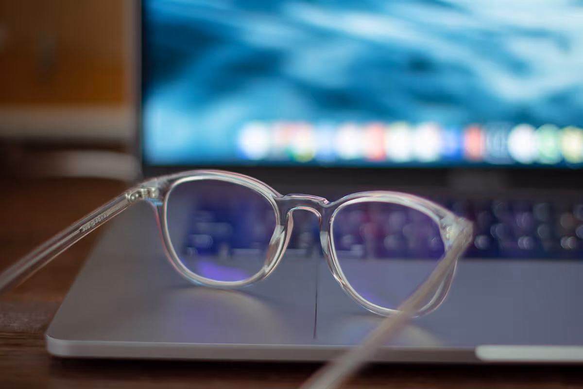 A pair of glasses in front of a computer monitor; pay transparency concept|Woman laughing behind laptop on desk