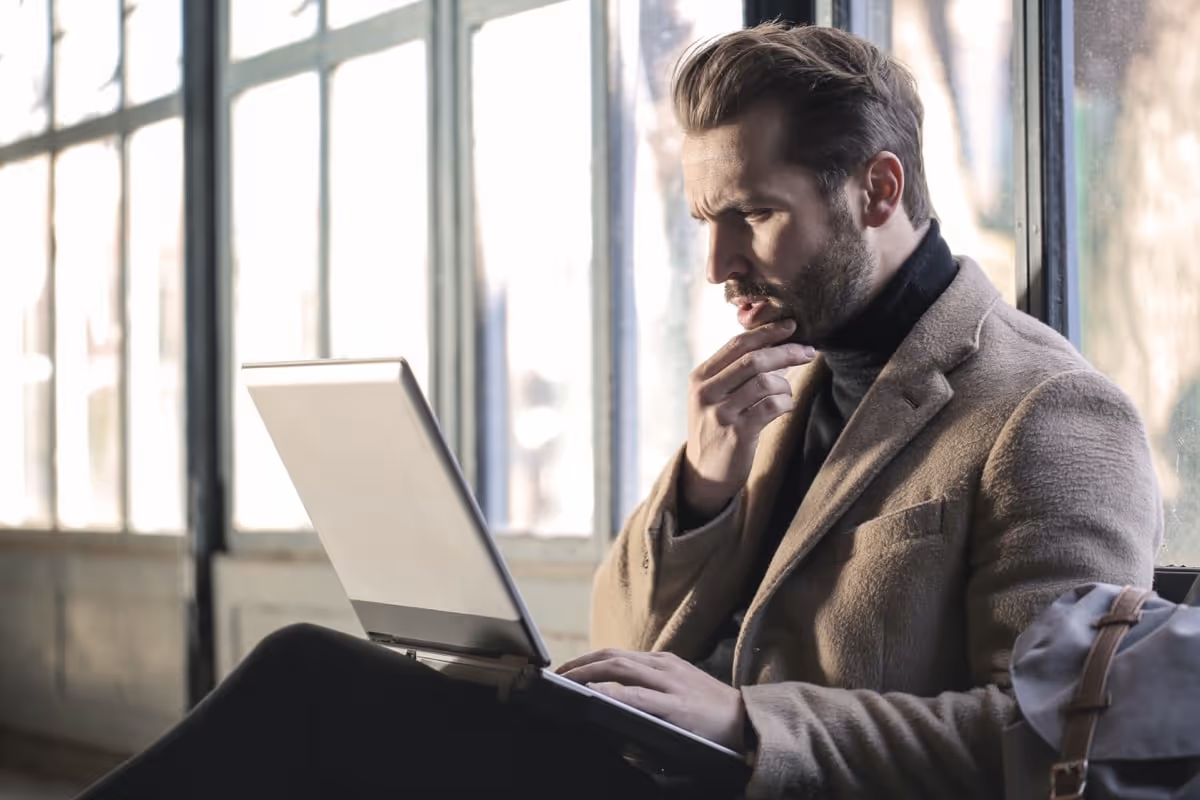 Bearded man looking pensively at laptop|Man scrolling through tablet on desk