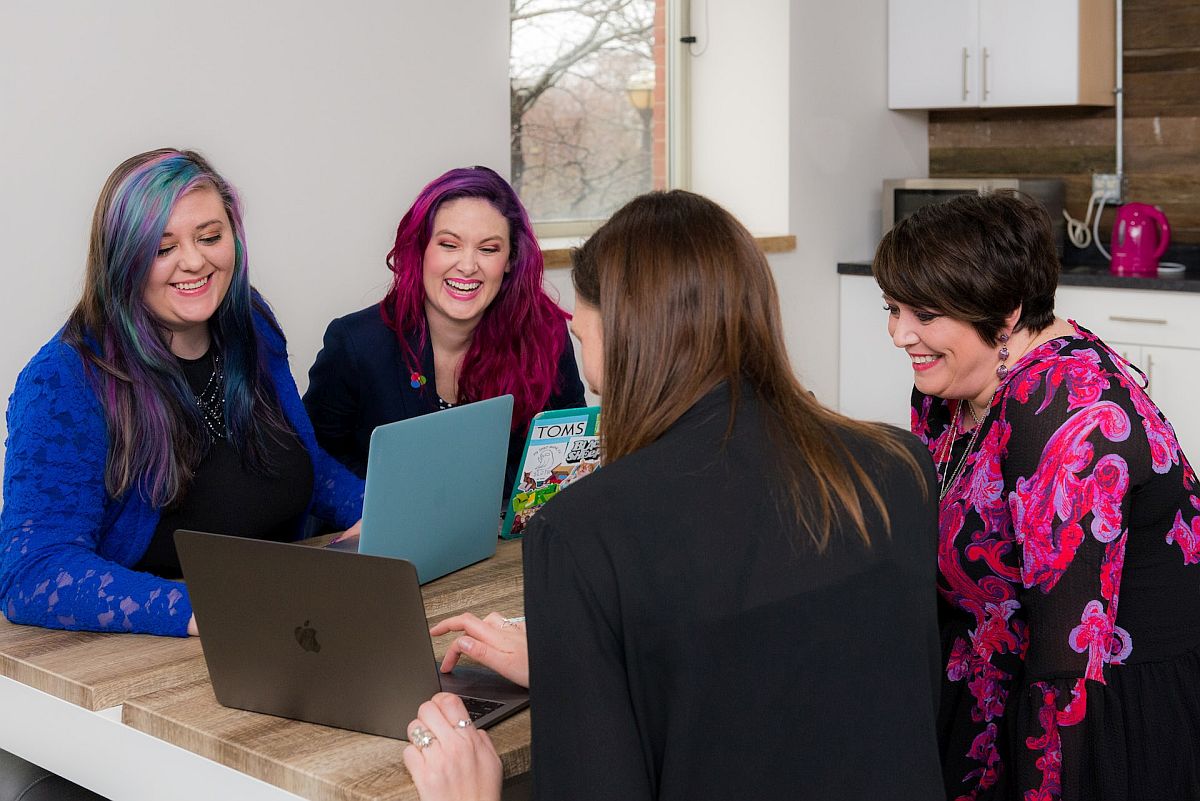 Group of women around a table, working on laptops; employee questions concept