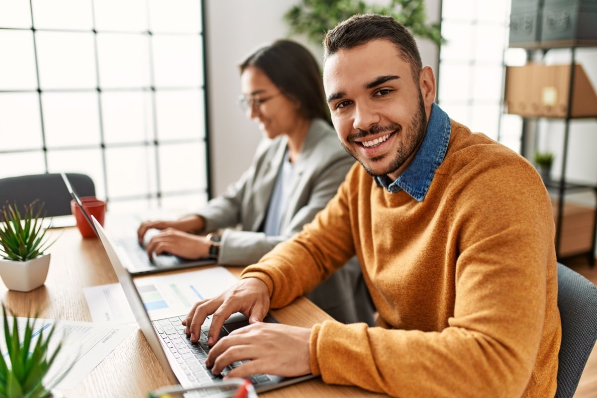 Two workers smiling happy working sitting on desk at the office; employee development concept