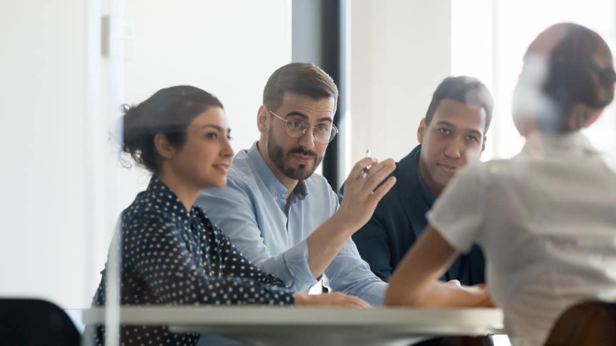 Serious team leader talking to female coworker sitting at conference room table; on-demand pay concept
