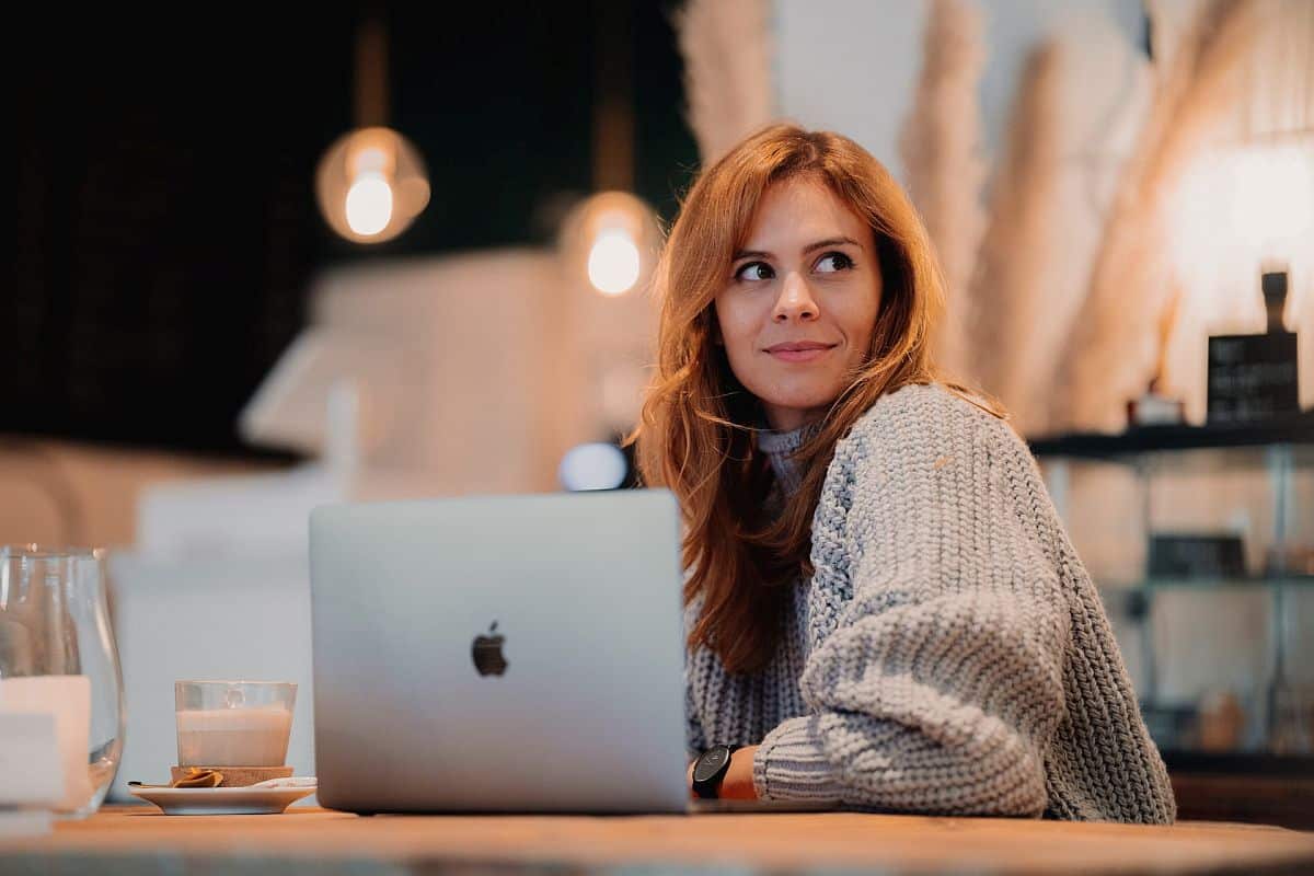 Smiling woman sitting in a cafe with her laptop open; effective rewards concept