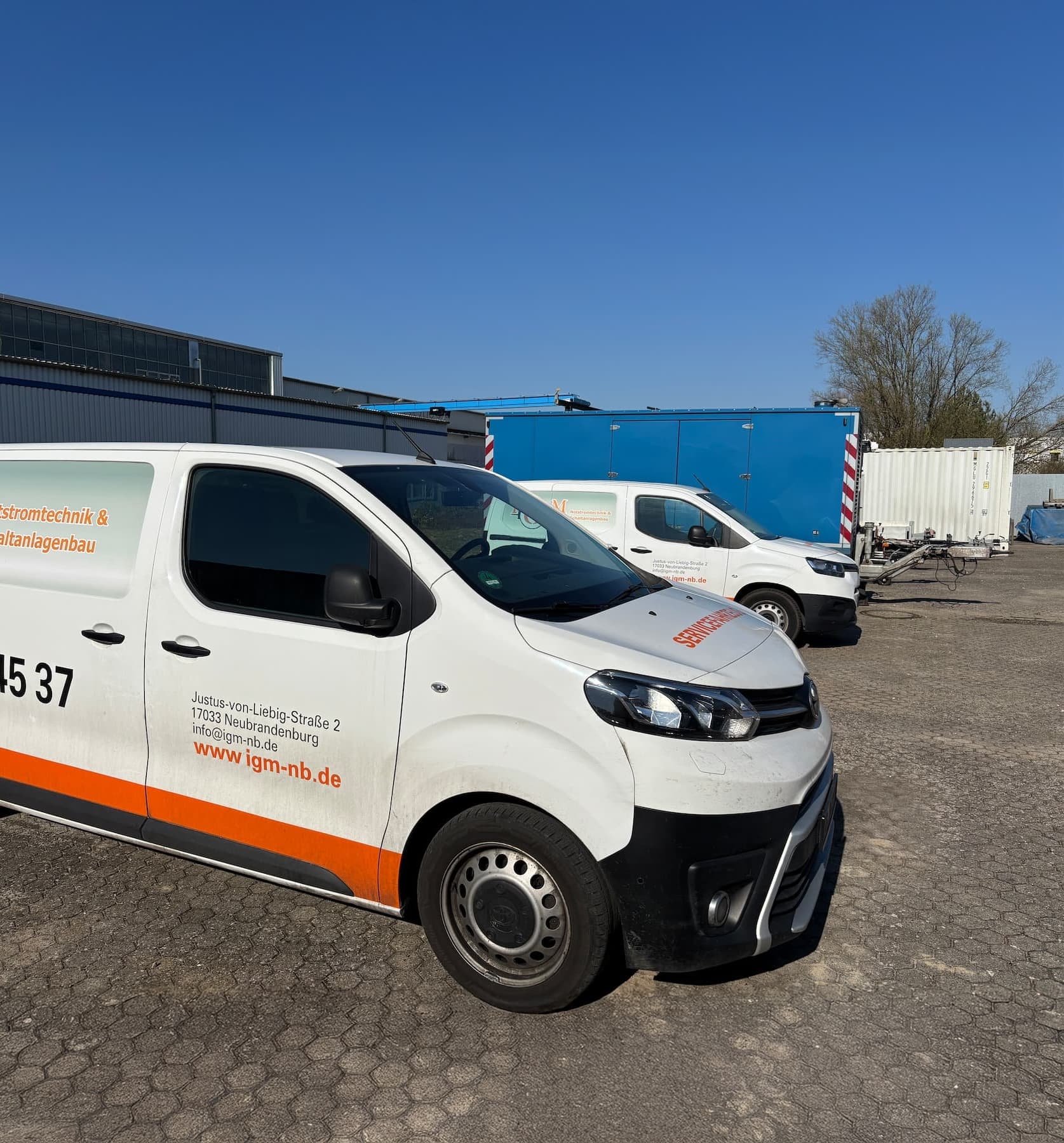 Zwei seitlich fotografierte Firmenfahrzeuge der IGM GmbH mit Beschriftung für Notstromtechnik und Schaltanlagenbau auf dem Firmenparkplatz
